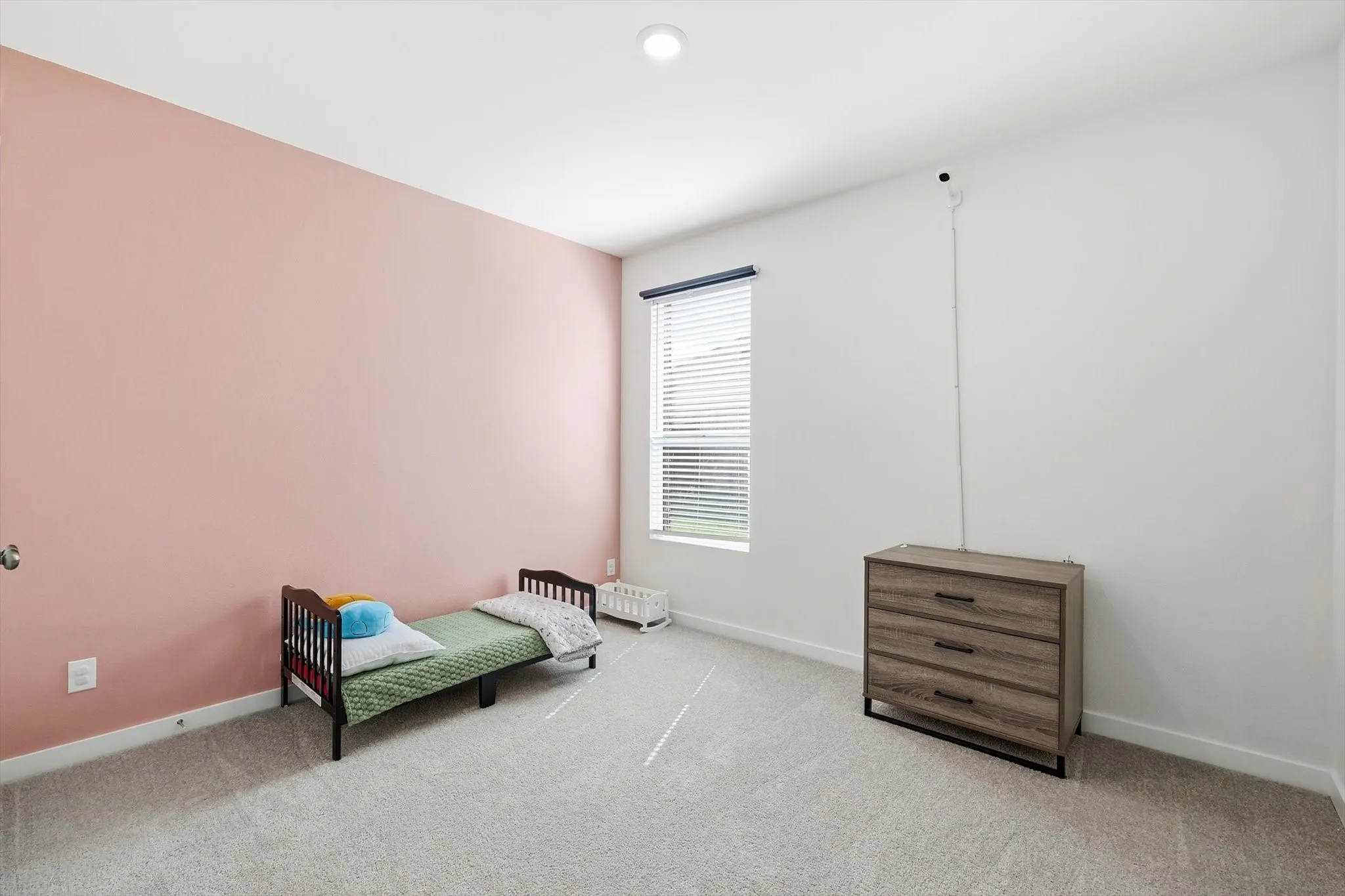 Spacious room featuring light-colored carpet, a large window with blinds, and a recessed ceiling light fixture