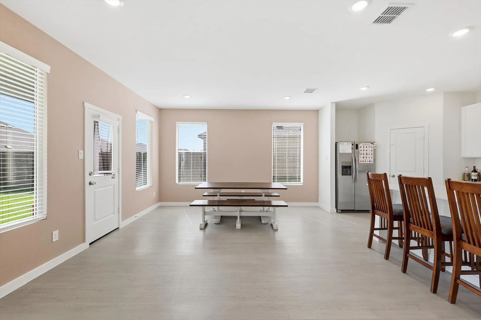 Open-concept living space featuring light-toned flooring, multiple windows with blinds, a white paneled door, and recessed lighting