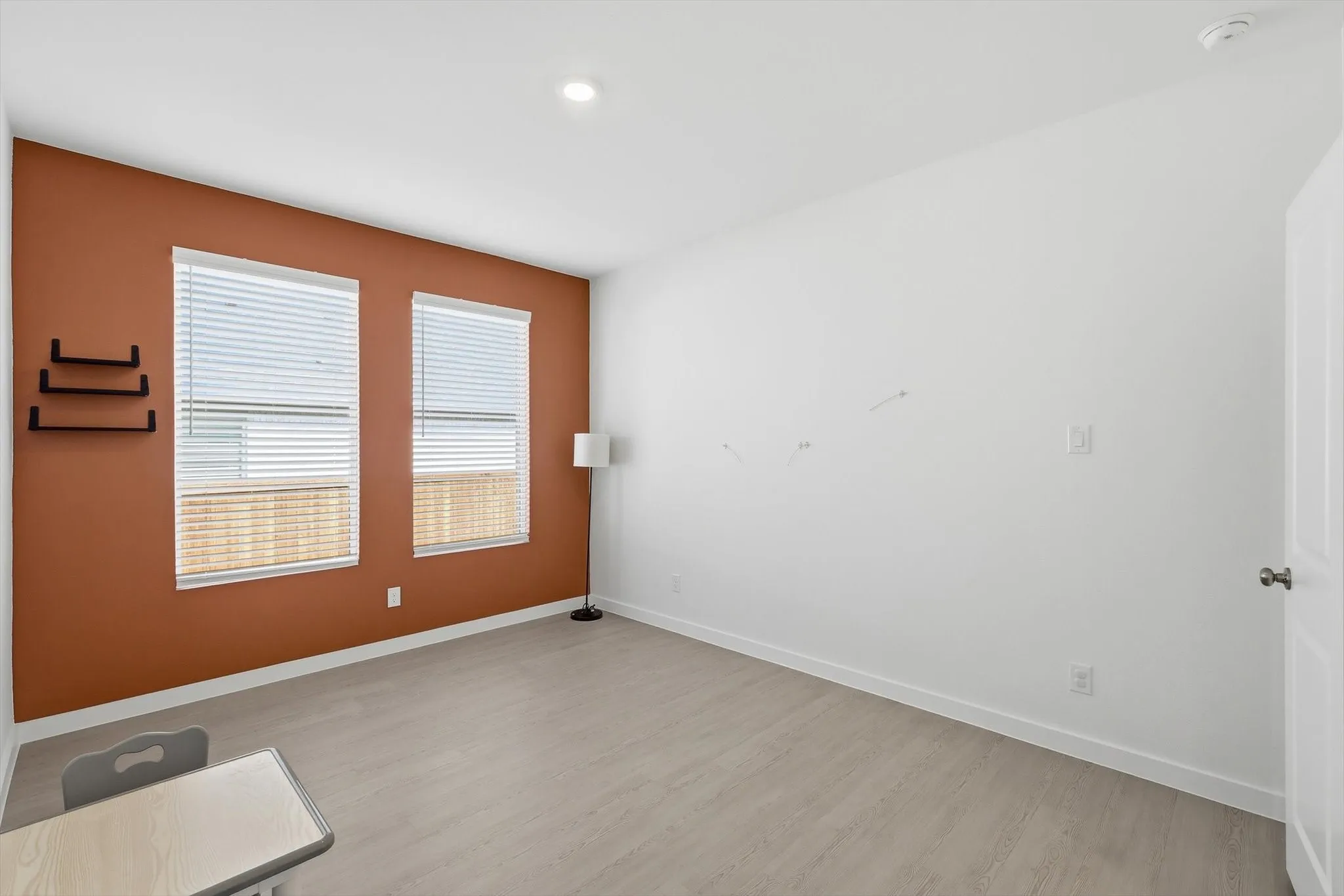 Bedroom featuring a warm accent wall, two window openings with blinds, and light wood-finish flooring
