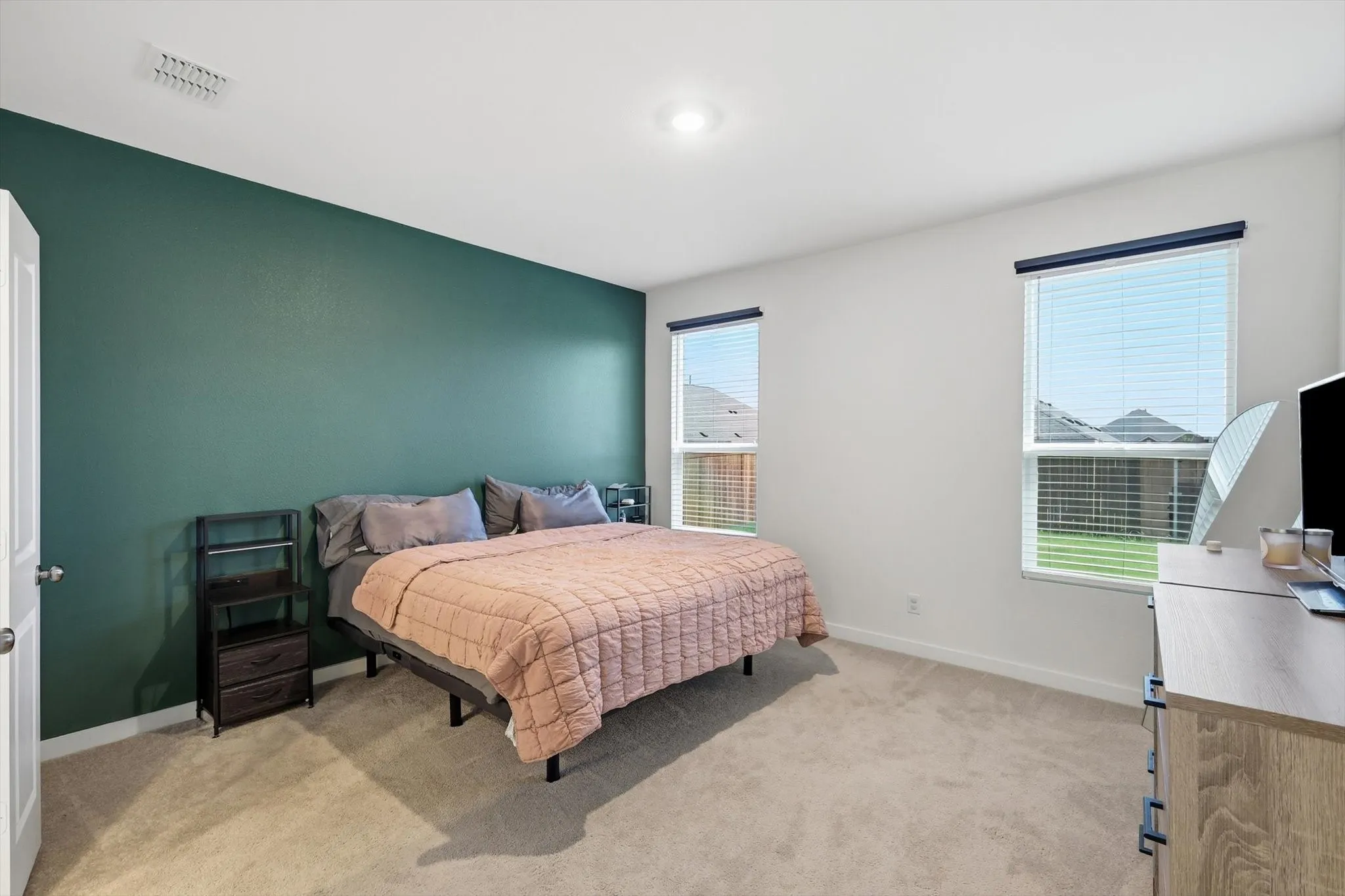 Bedroom featuring a dark teal accent wall, neutral carpeting, and two windows with blinds