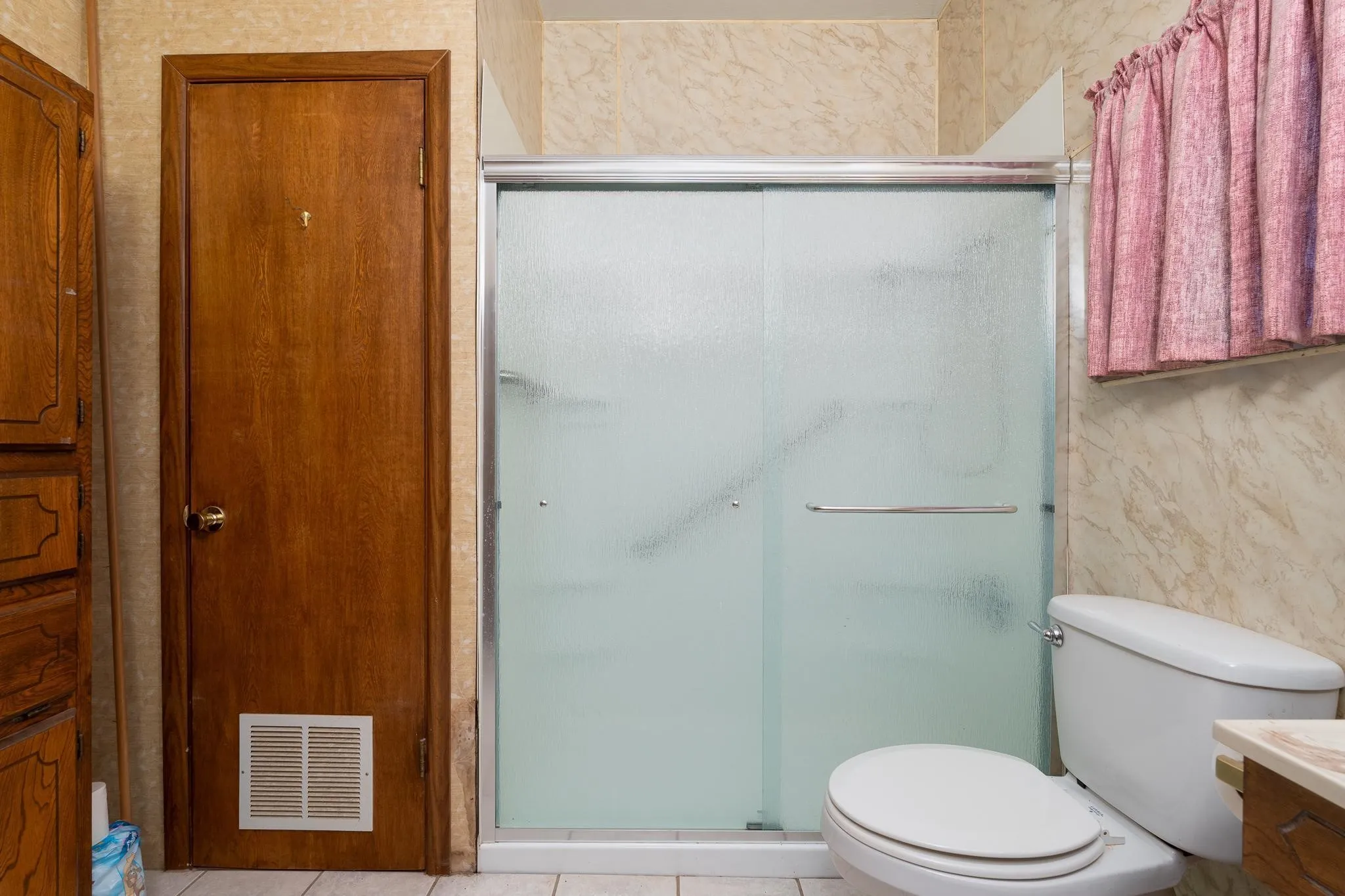 Shower enclosure with frosted glass sliding doors, a white porcelain toilet, and a wood-finish door