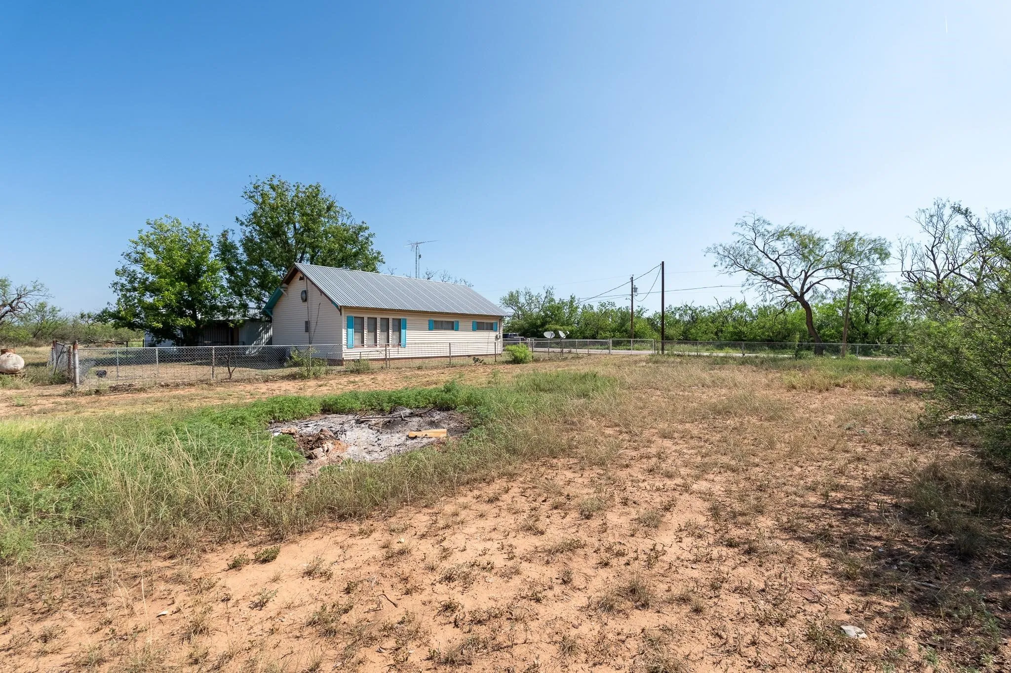 Property exterior featuring a light-colored facade with blue shutters, a pitched metal roof, and a fenced perimeter