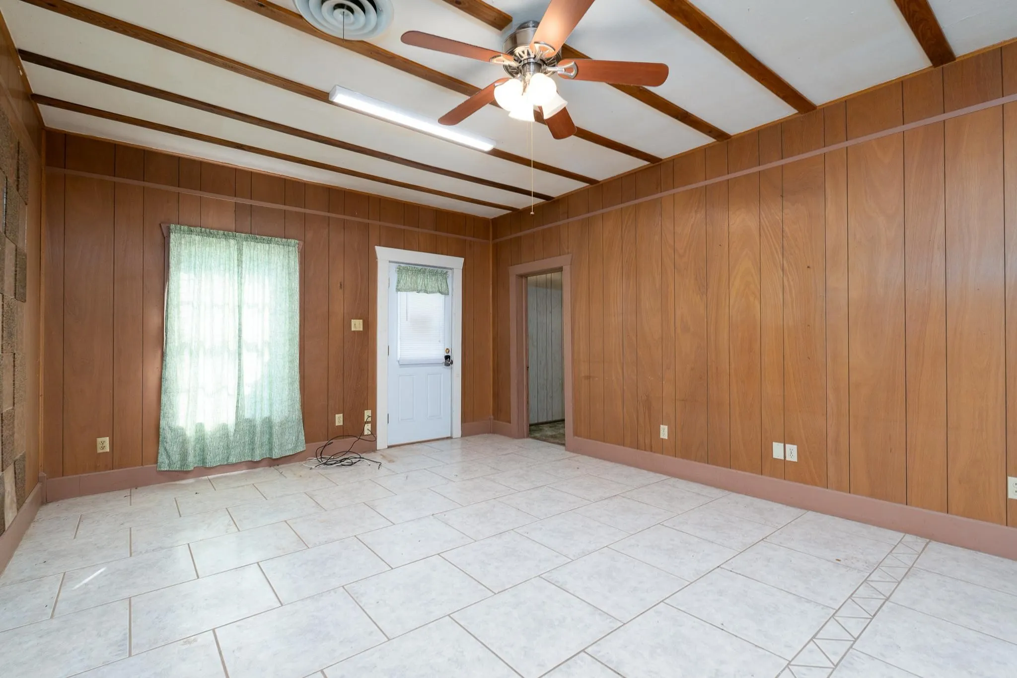 Spacious room featuring wood paneling, white tiled flooring, and a beamed ceiling