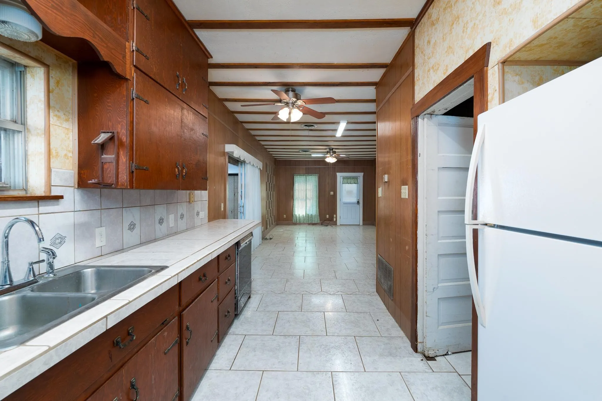 Kitchen area featuring wood cabinetry, a dual basin stainless steel sink, and a tiled countertop with coordinating backsplash
