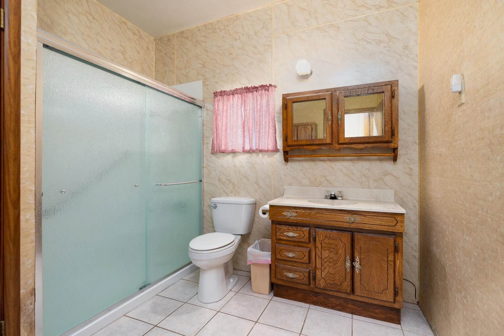 Bathroom featuring a shower with frosted glass doors, a single vanity with wood cabinetry, and a mirrored medicine cabinet