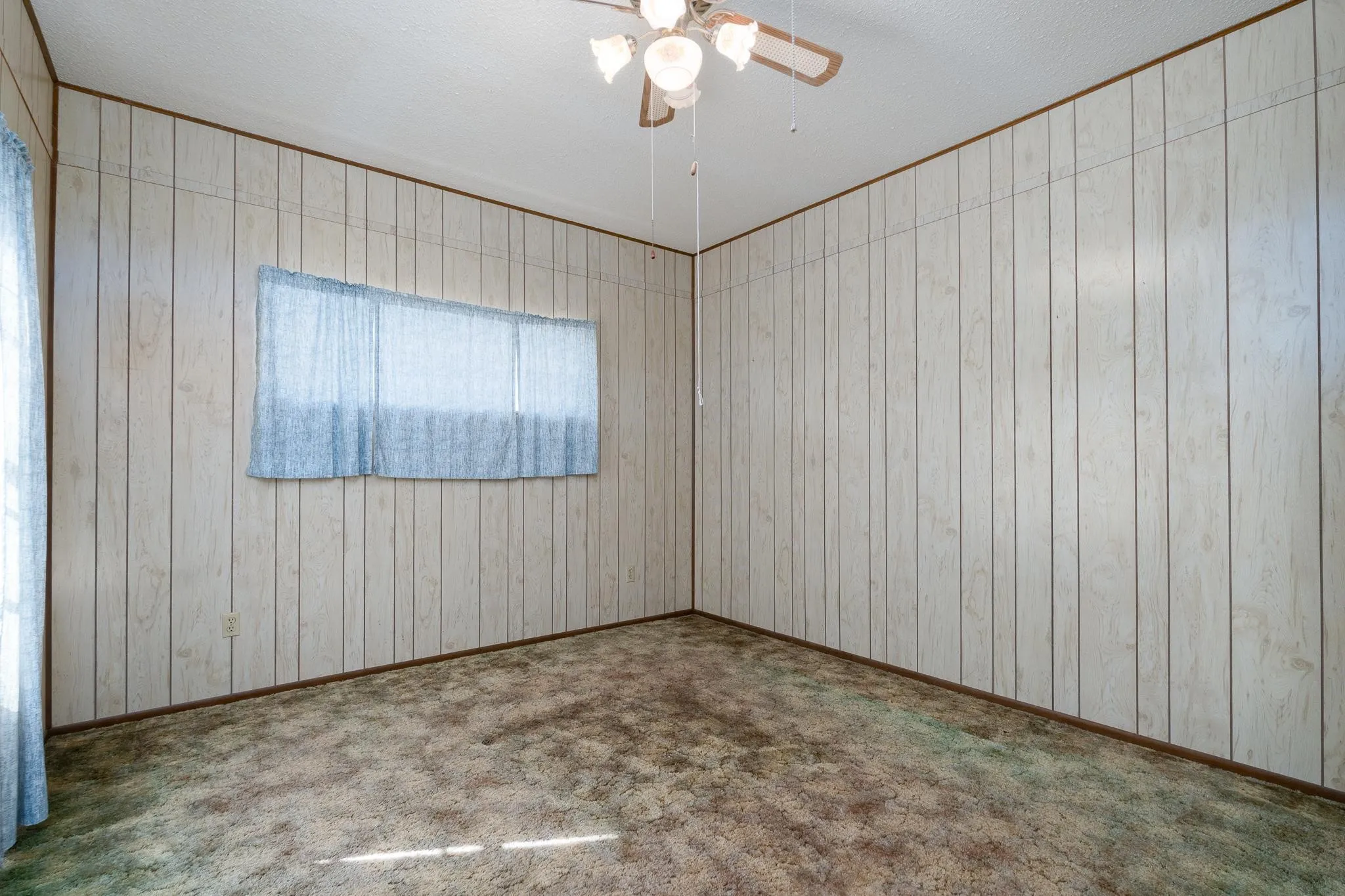 Room featuring white wood-panel walls, patterned carpet flooring, and a ceiling fan with light fixture