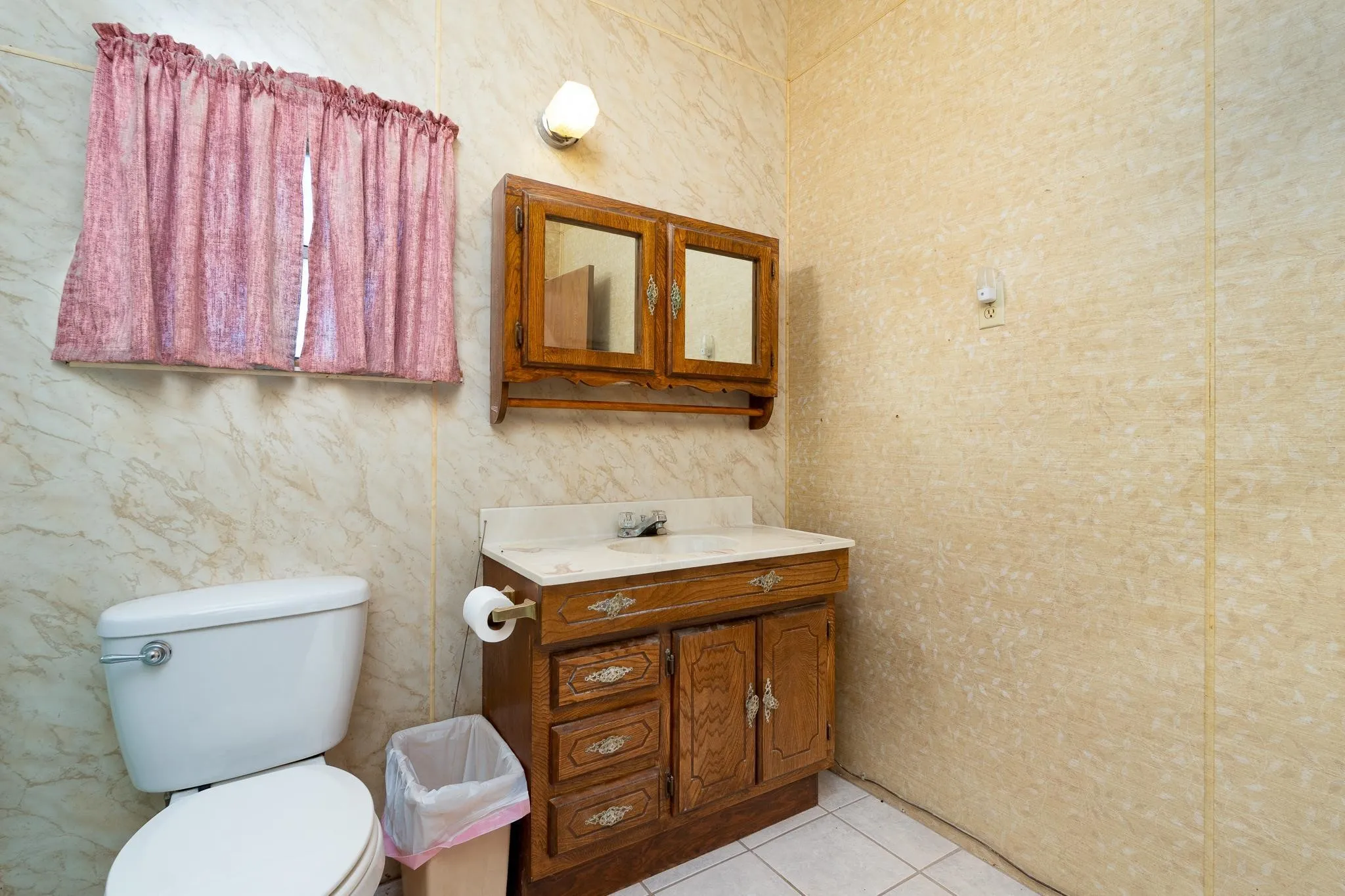 Bathroom featuring a white toilet, wood-finish vanity with an integrated sink and white countertop, and a matching wood-finish medicine cabinet with mirrored doors