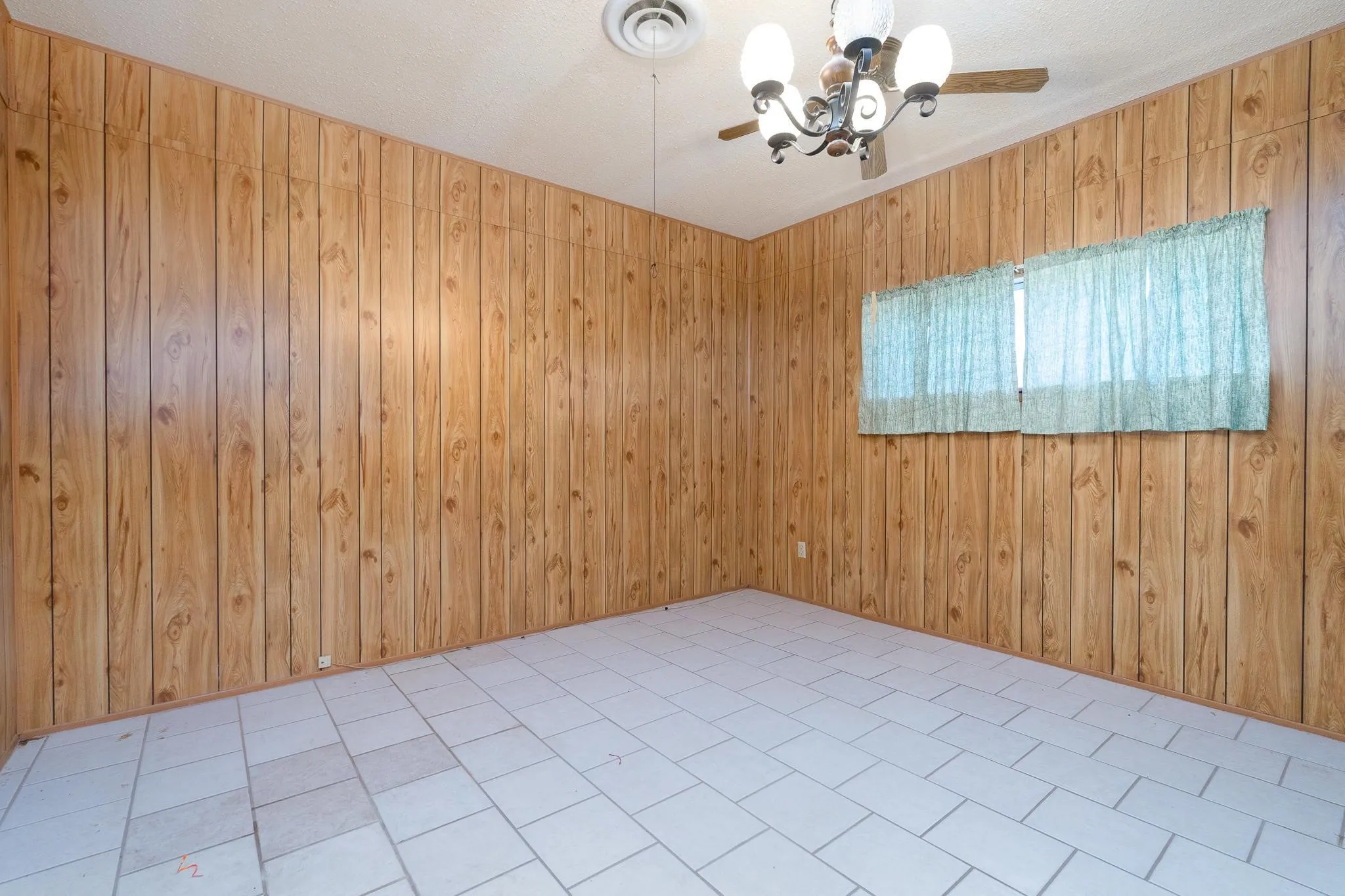 Room featuring wood-finish paneling, light-colored tile flooring, a window with curtains, and a ceiling fan with integrated lighting