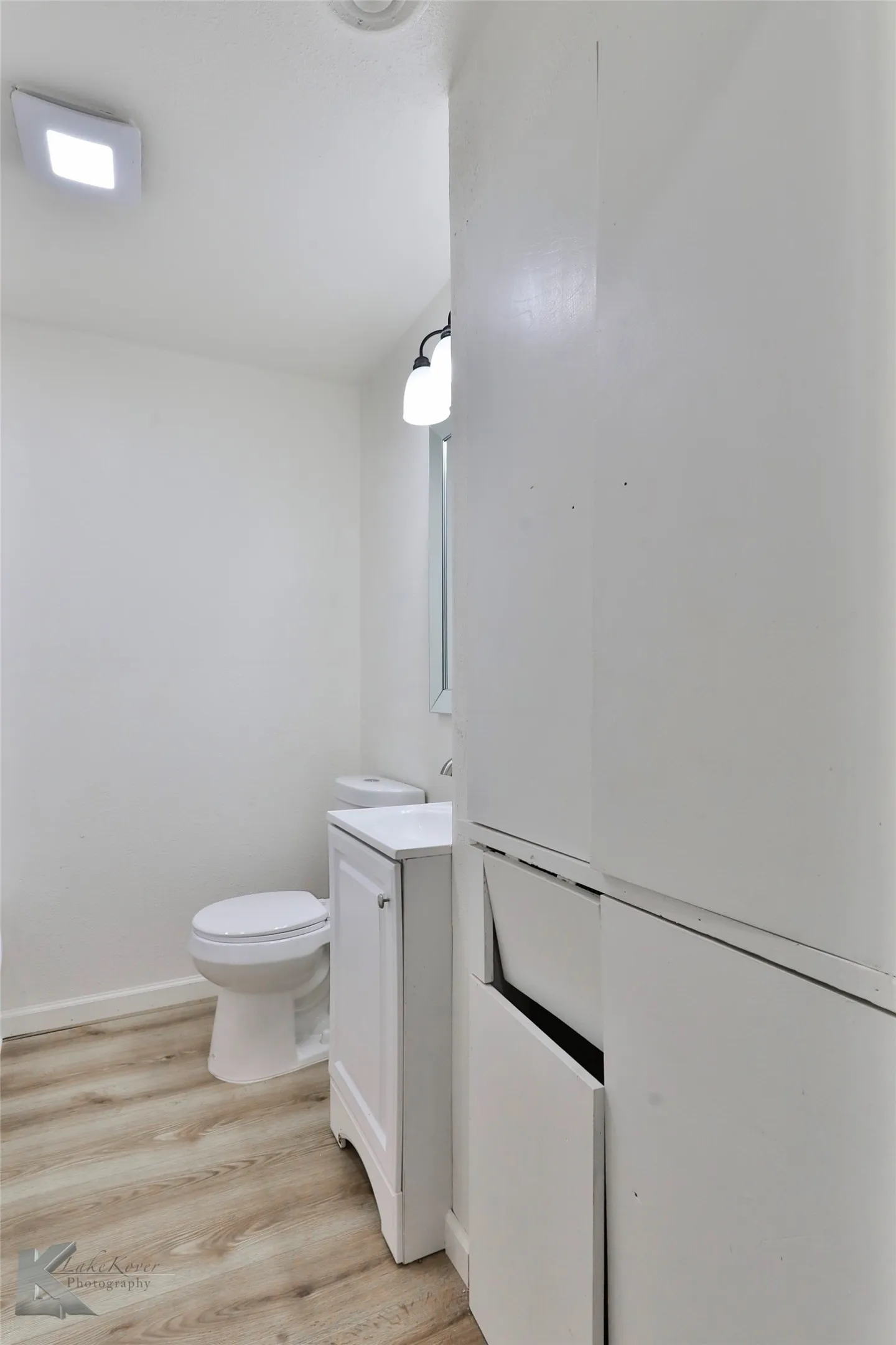 Bathroom featuring light wood-finish flooring, white vanity with integrated sink, white toilet, and built-in white cabinetry