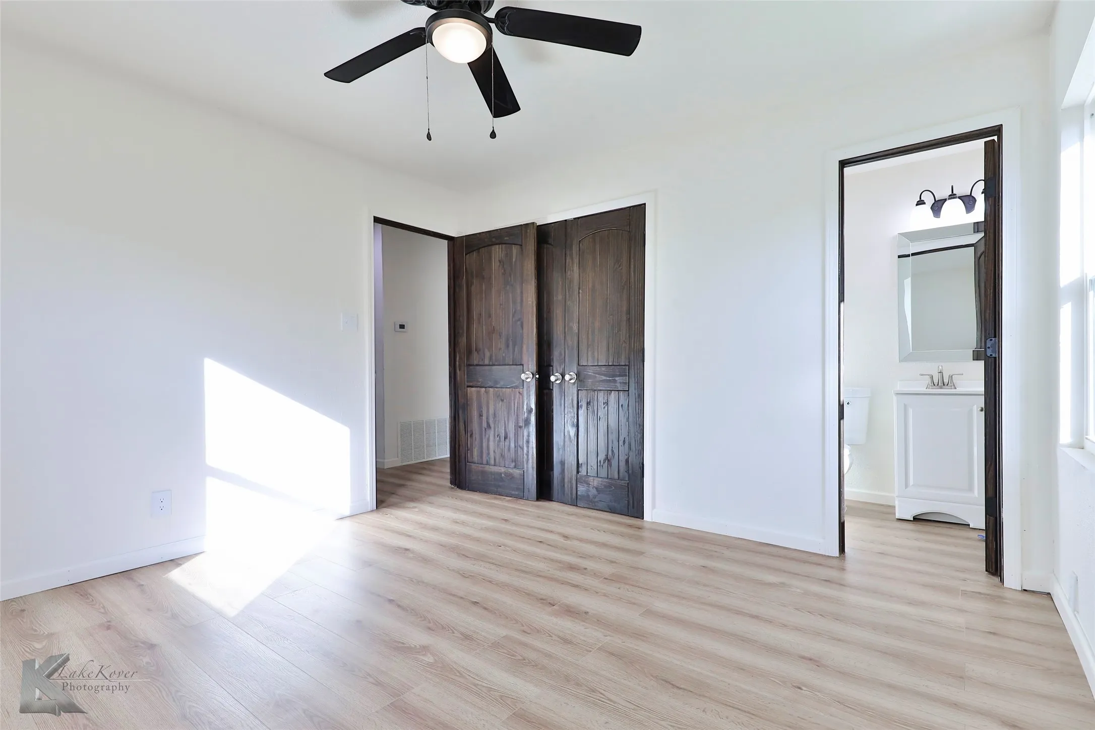 Spacious room featuring wood-finish flooring and a black ceiling fan with integrated lighting
