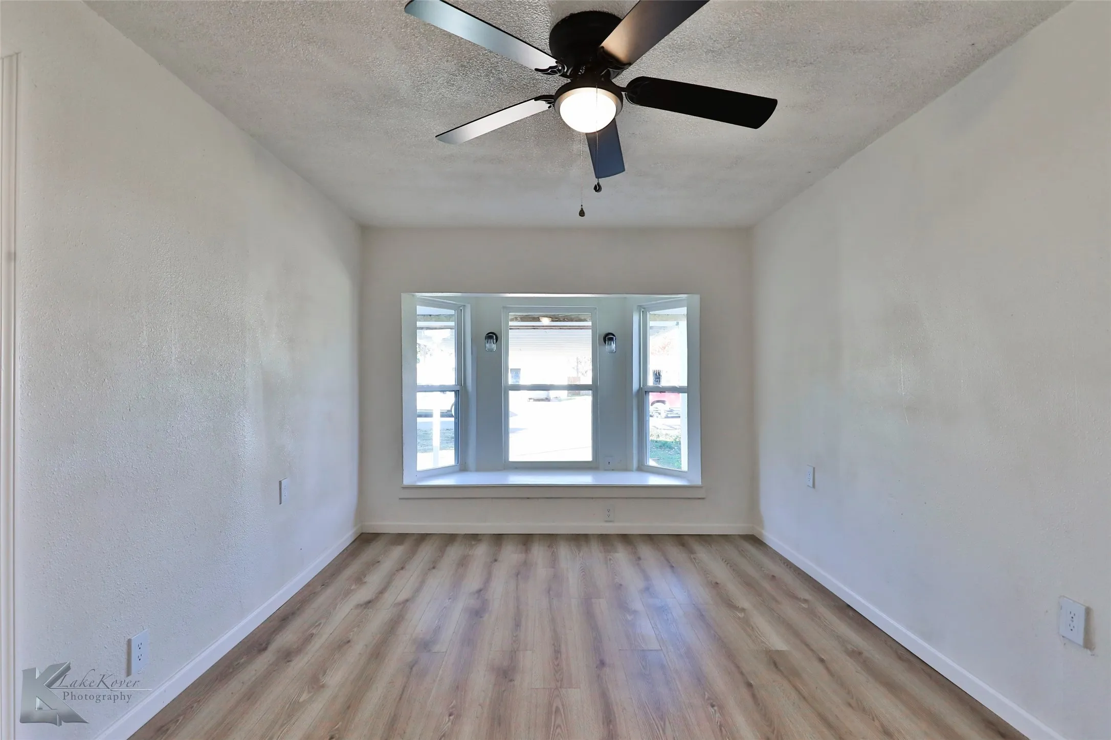 Room featuring a bay window with a deep sill, wood-finish flooring, a ceiling fan with integrated lighting, and white walls