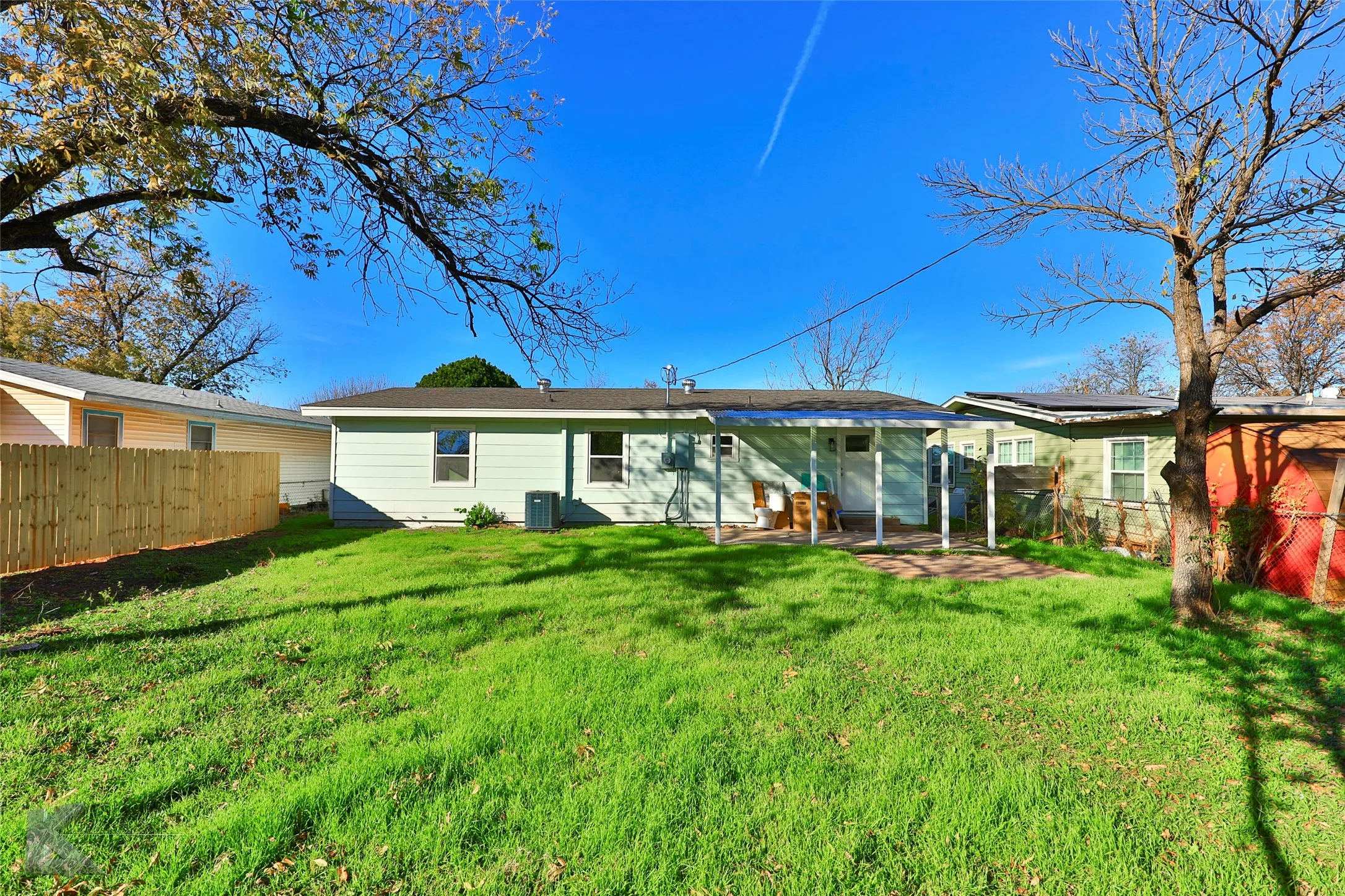 Expansive green lawn with a covered patio, paved outdoor area, and a newly installed wood fence