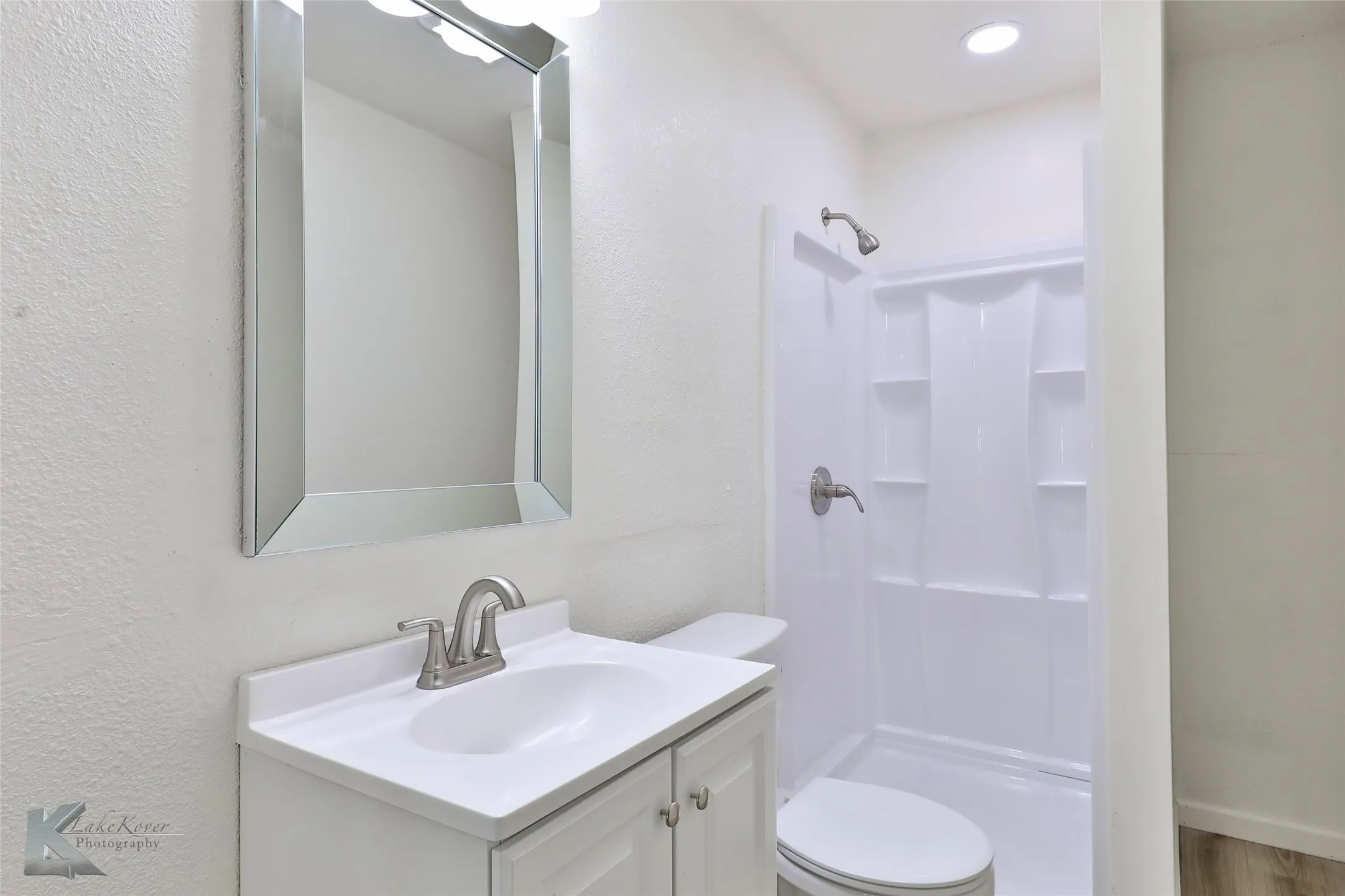 White vanity with a brushed nickel faucet, an integrated sink, and an unframed mirror