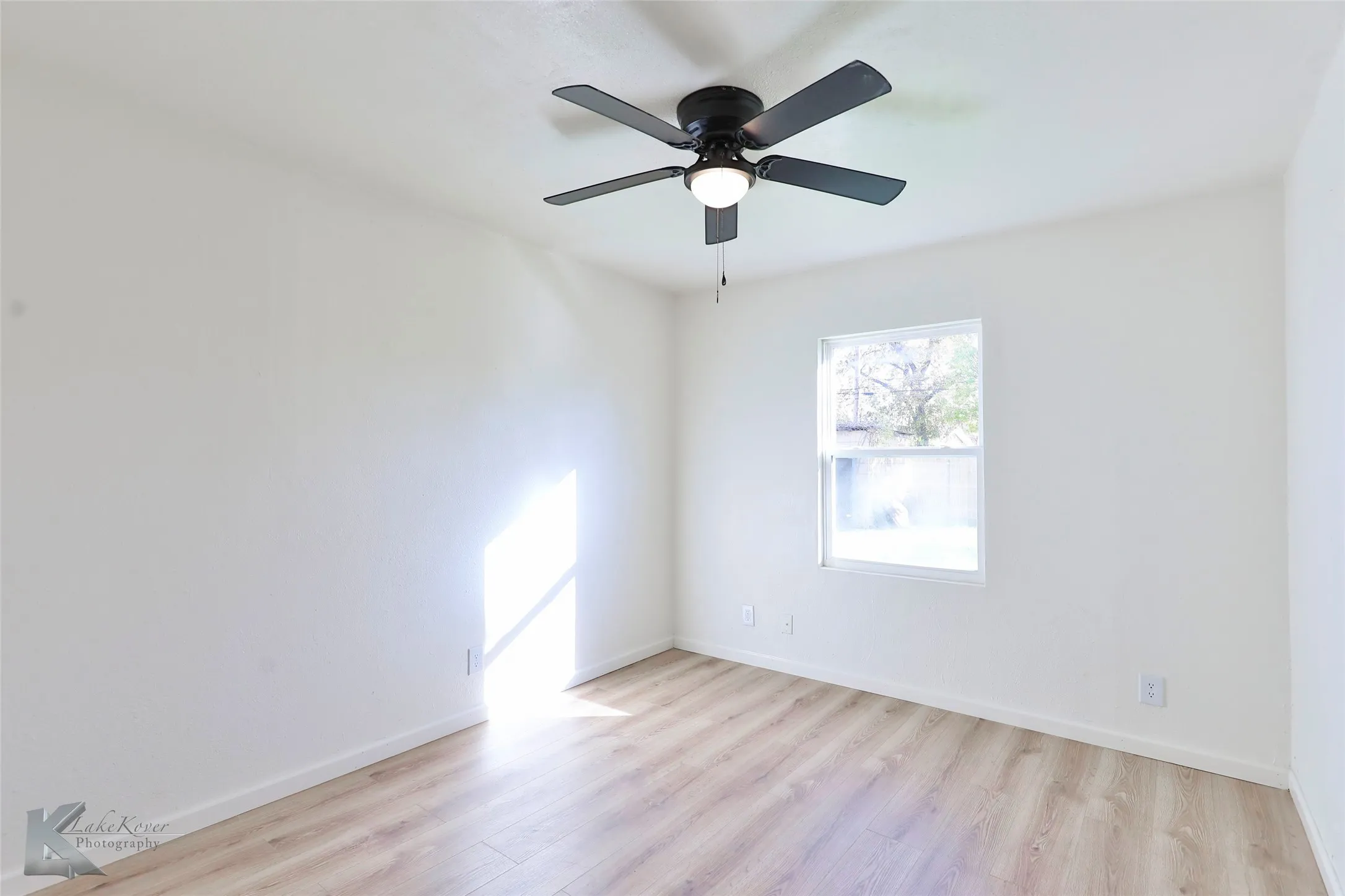 Bright interior space featuring a window, wood-finish flooring, a ceiling fan with integrated lighting, and neutral wall finishes