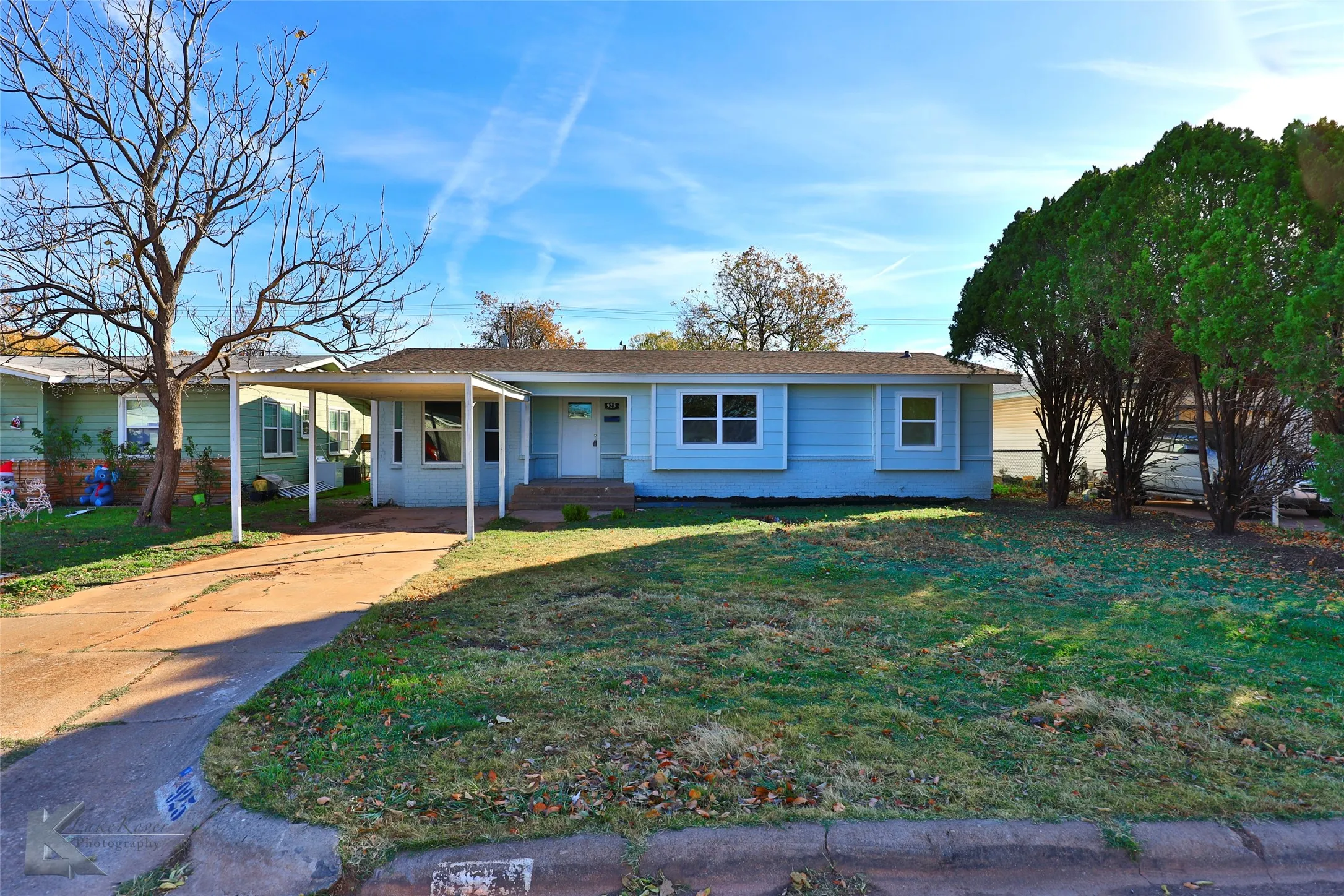 Light blue siding exterior featuring a covered carport, concrete driveway, and a front lawn