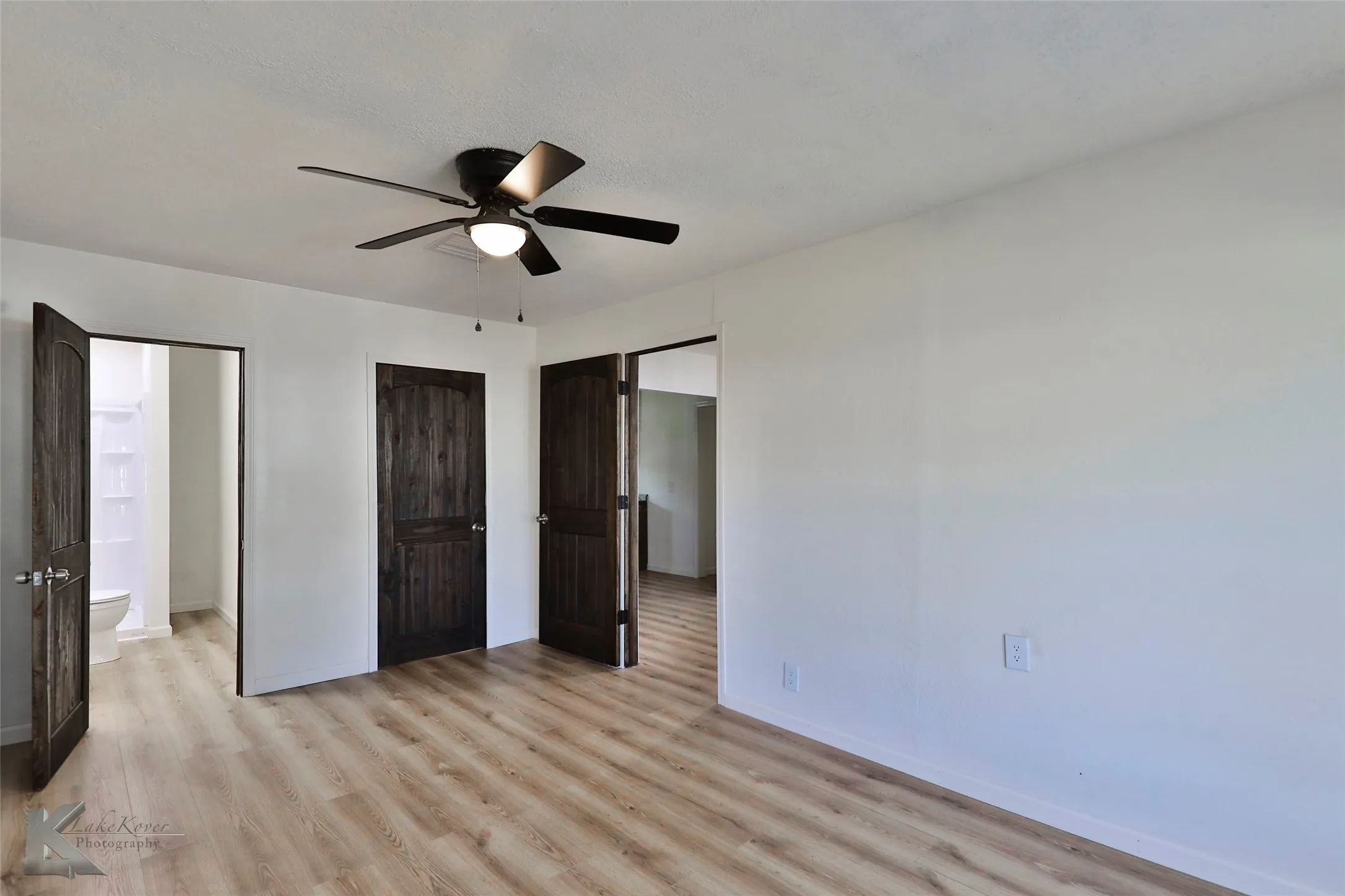 Interior room featuring wood-finish flooring, white walls, and a dark-toned ceiling fan