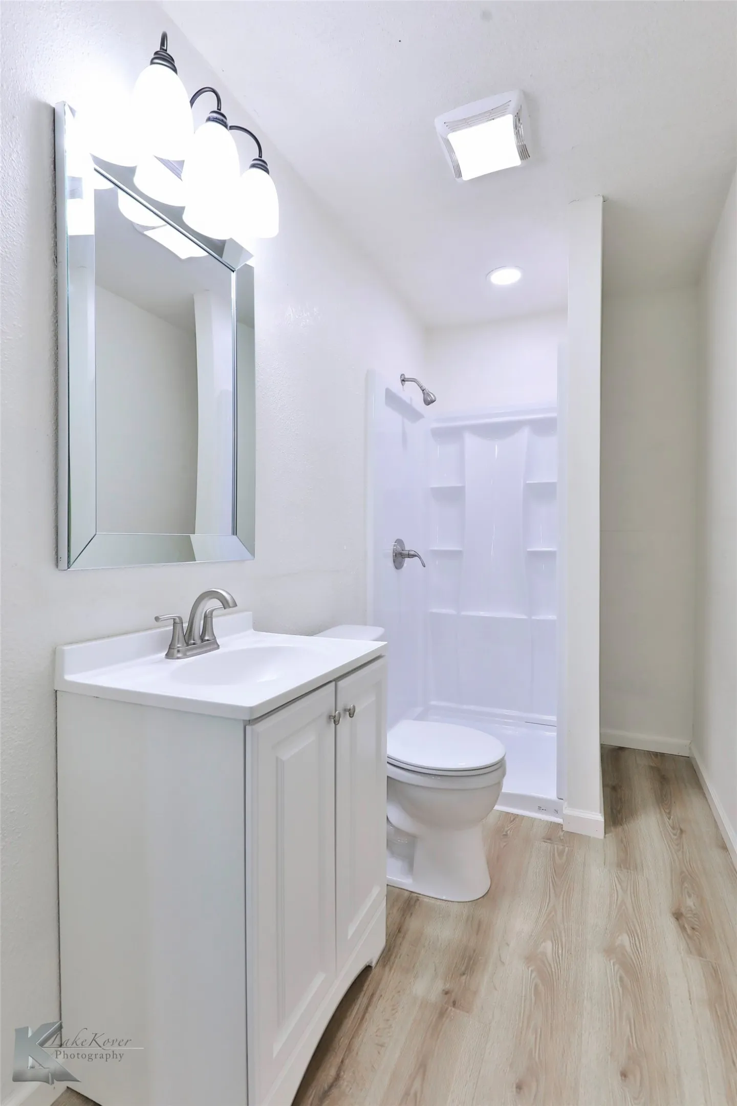 Bathroom featuring wood-finish flooring, a white vanity with integrated sink, brushed nickel faucet, and a rectangular mirrored vanity