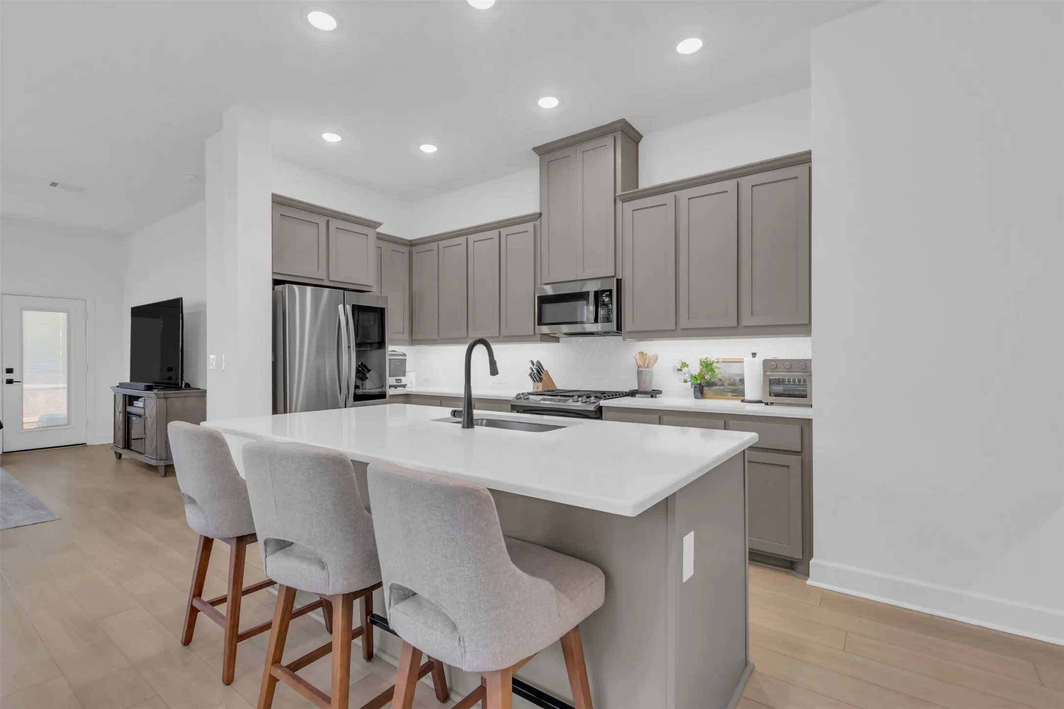 Kitchen featuring a large island with white countertop, gray cabinetry, stainless steel appliances, and wood-finish flooring