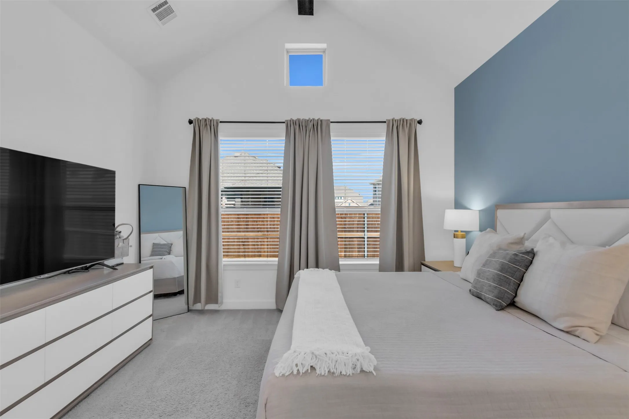 Vaulted ceiling bedroom featuring a high window, two large windows with horizontal blinds, and carpet flooring