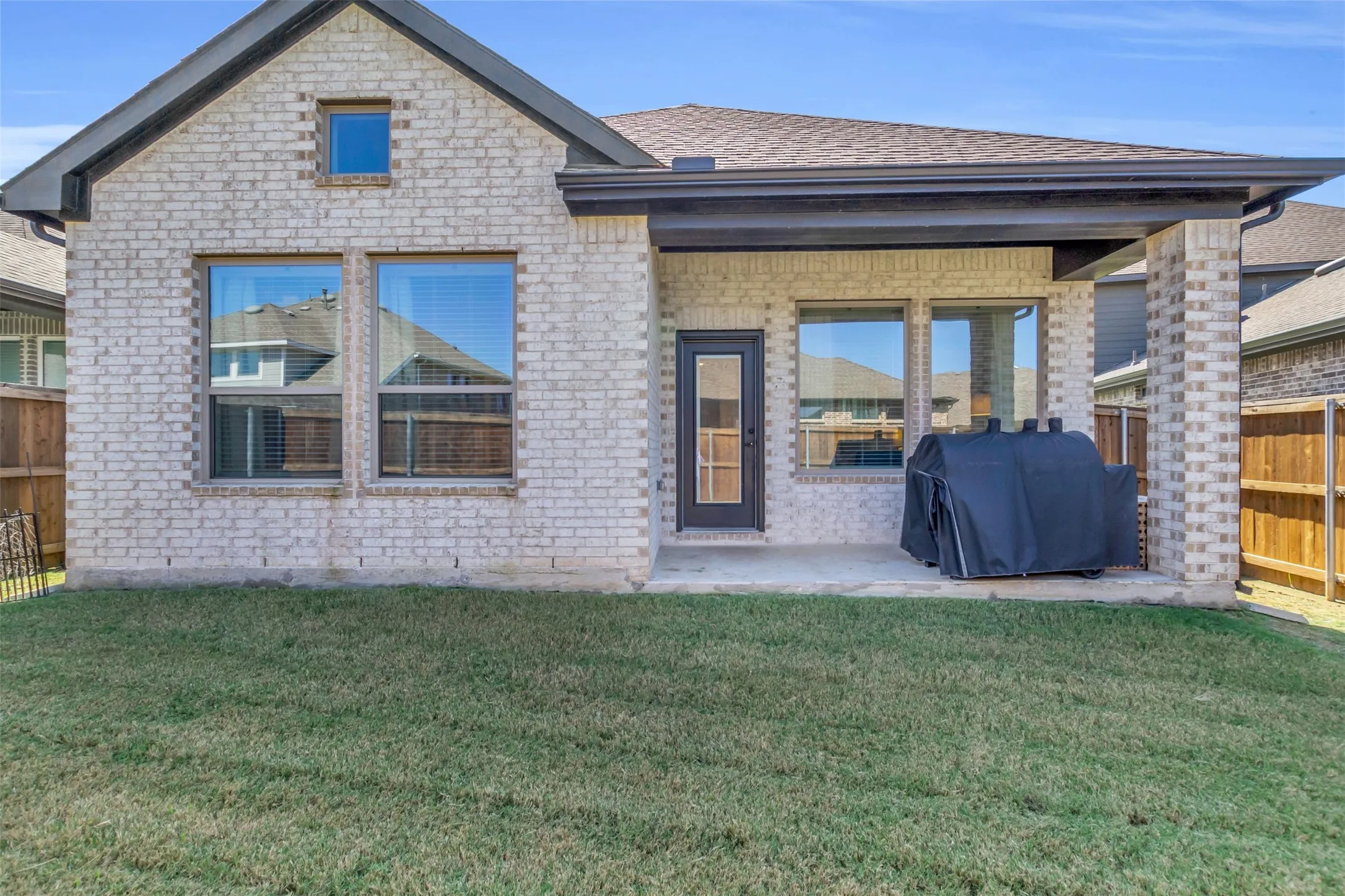 Exterior features include a light-colored brick facade, a covered patio, and a grass lawn