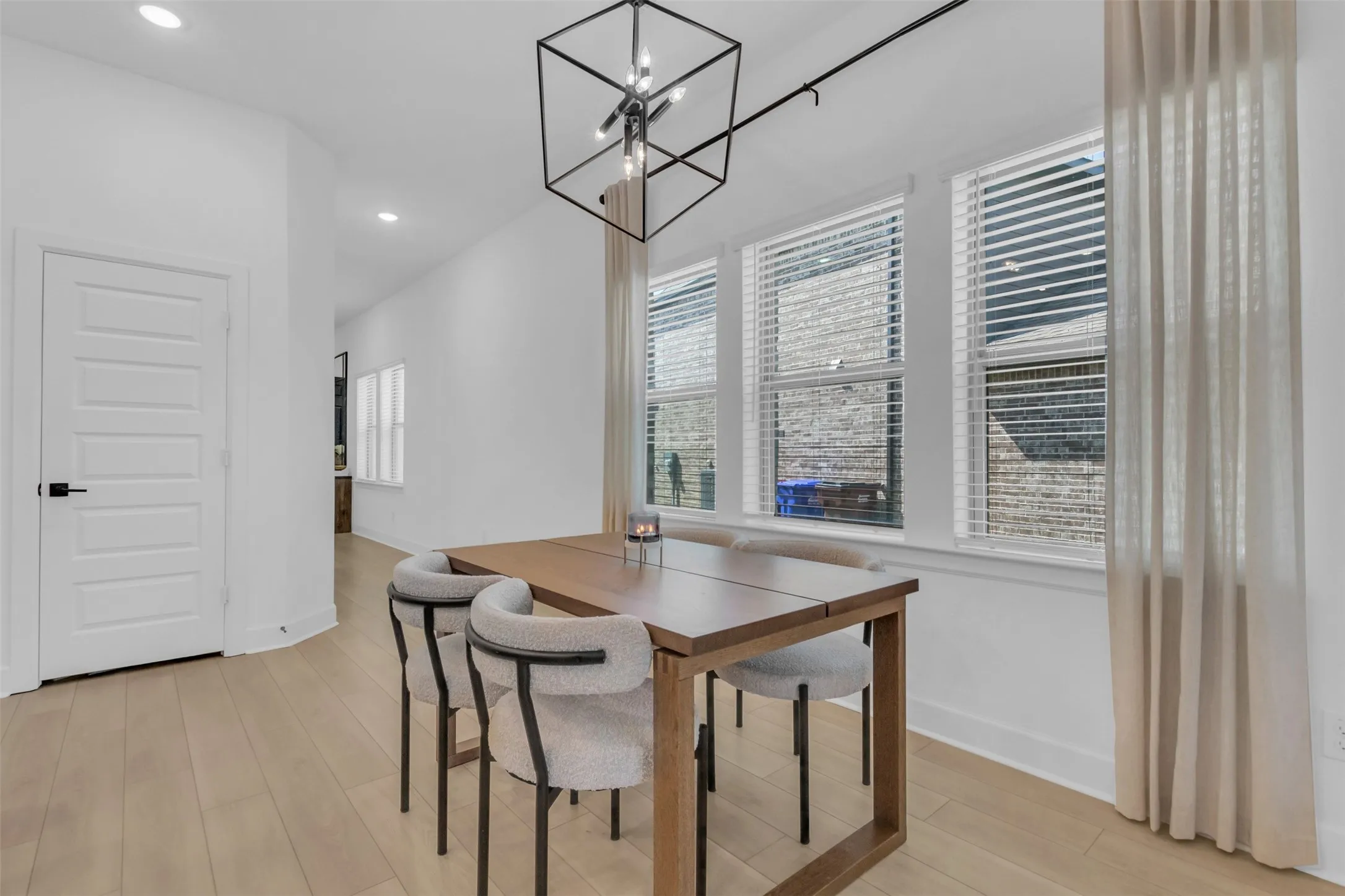 Dining area featuring wood-finish flooring, a contemporary geometric chandelier, and multiple windows with blinds
