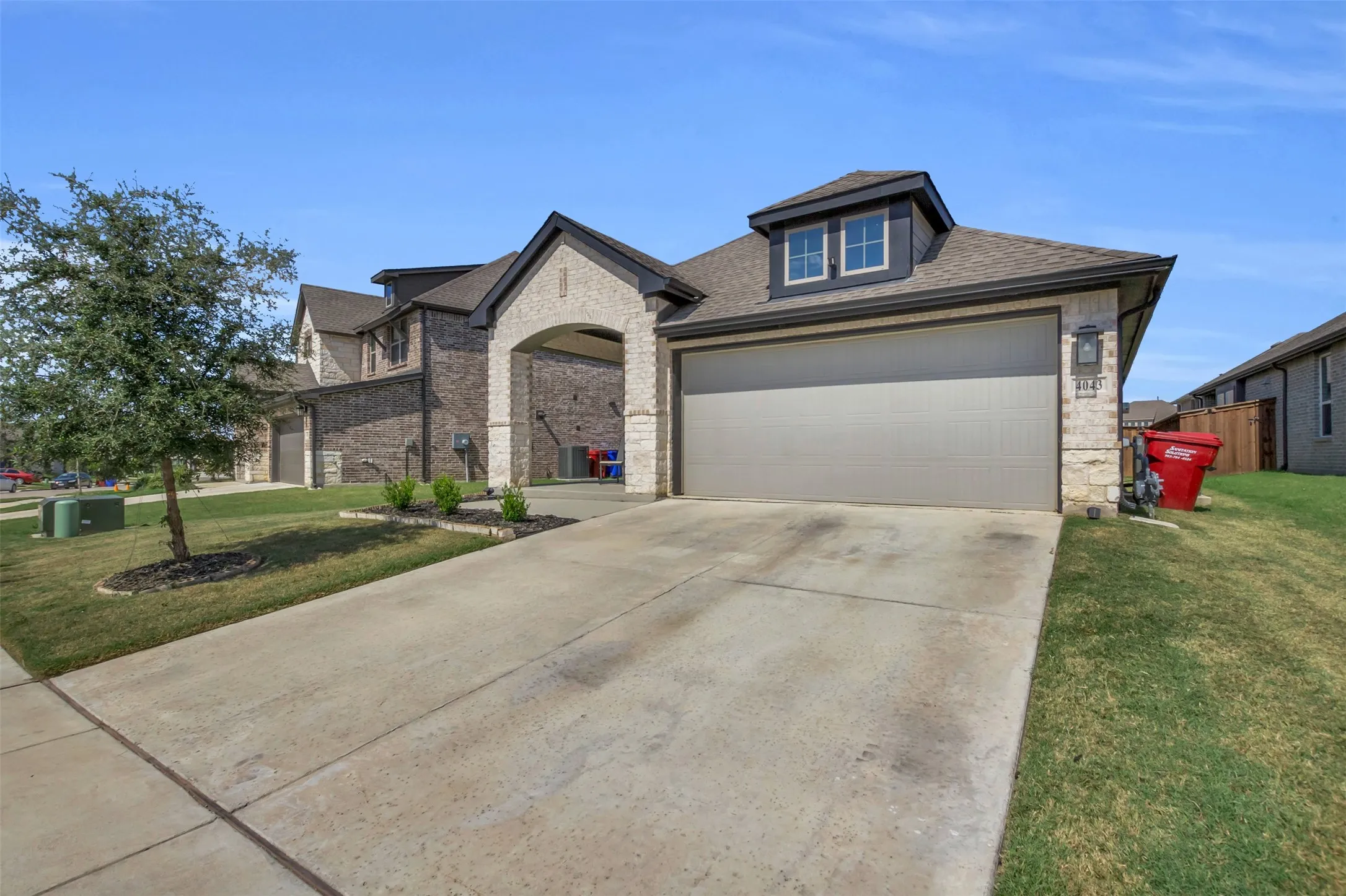 Contemporary exterior featuring a combination of brick and stone masonry, an attached two-car garage, and a dormer window