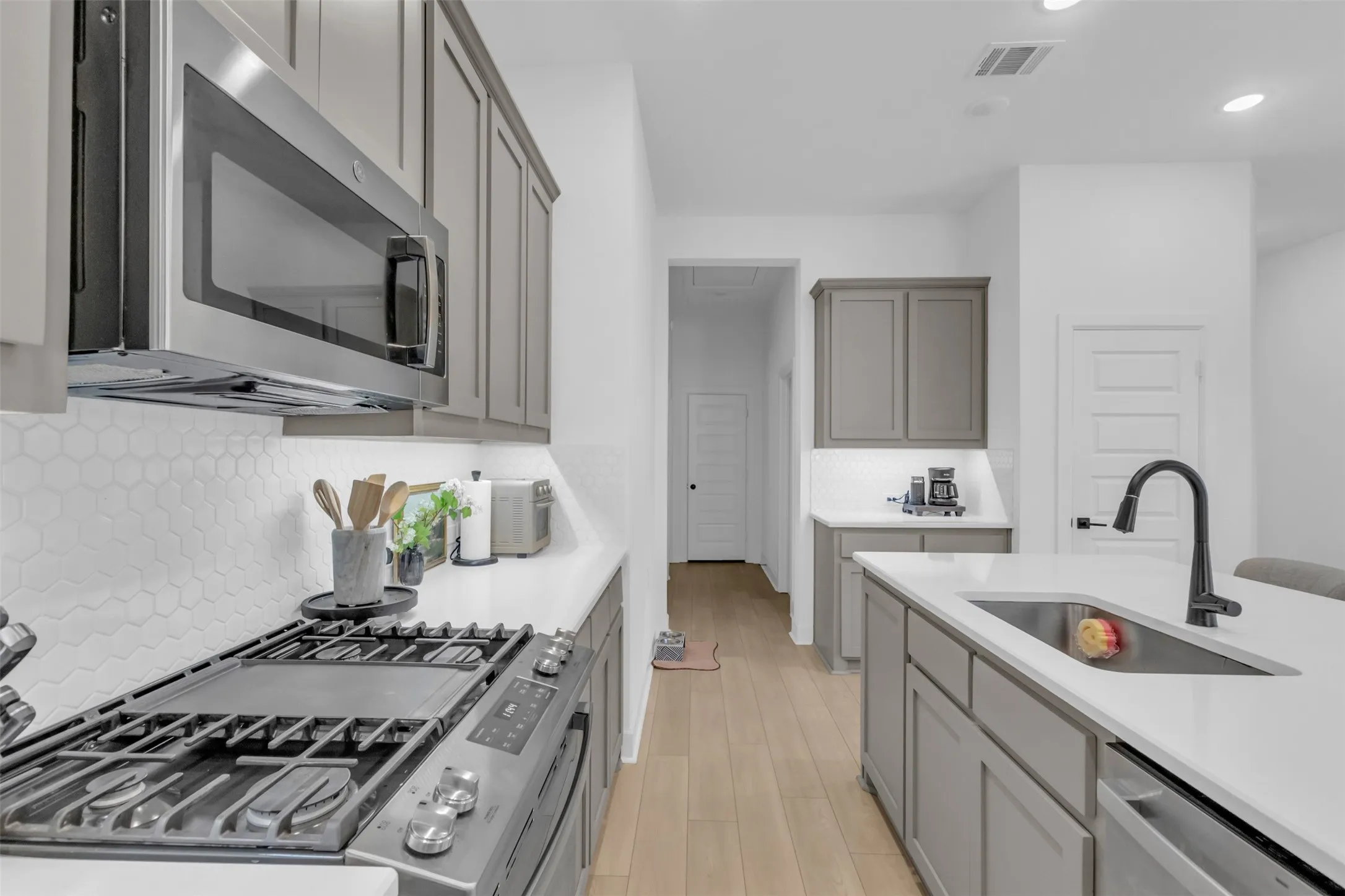 Contemporary kitchen featuring light gray cabinetry, white countertops, wood-finish flooring, stainless steel appliances, and a hexagonal tile backsplash