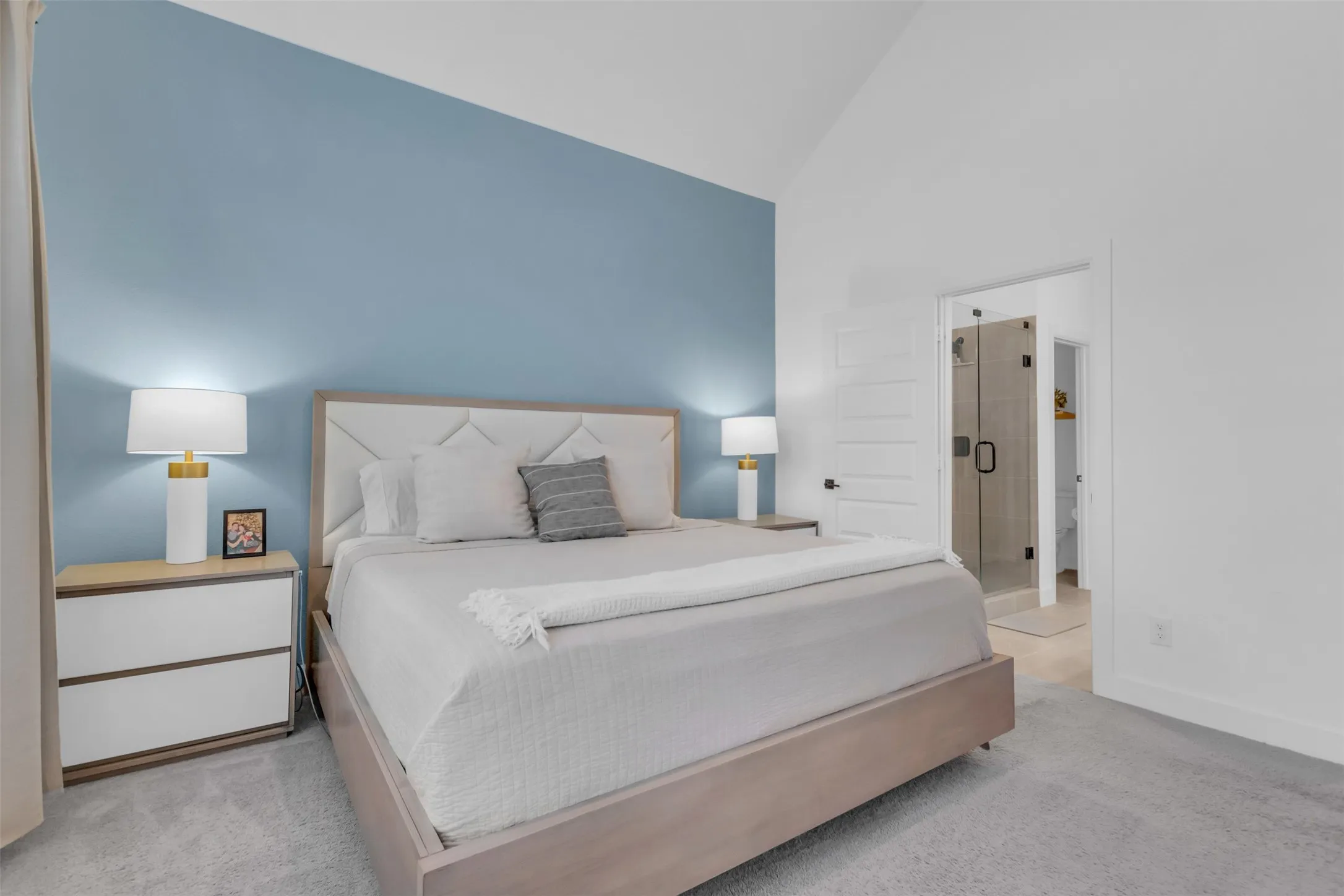 Vaulted ceiling bedroom featuring a feature wall, plush carpeting, and direct access to an en-suite with a frameless glass shower enclosure