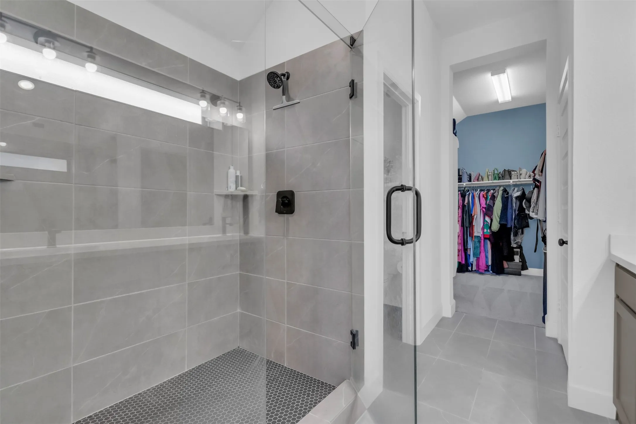 Glass-enclosed shower with large format grey wall tiles and dark penny round floor tiles