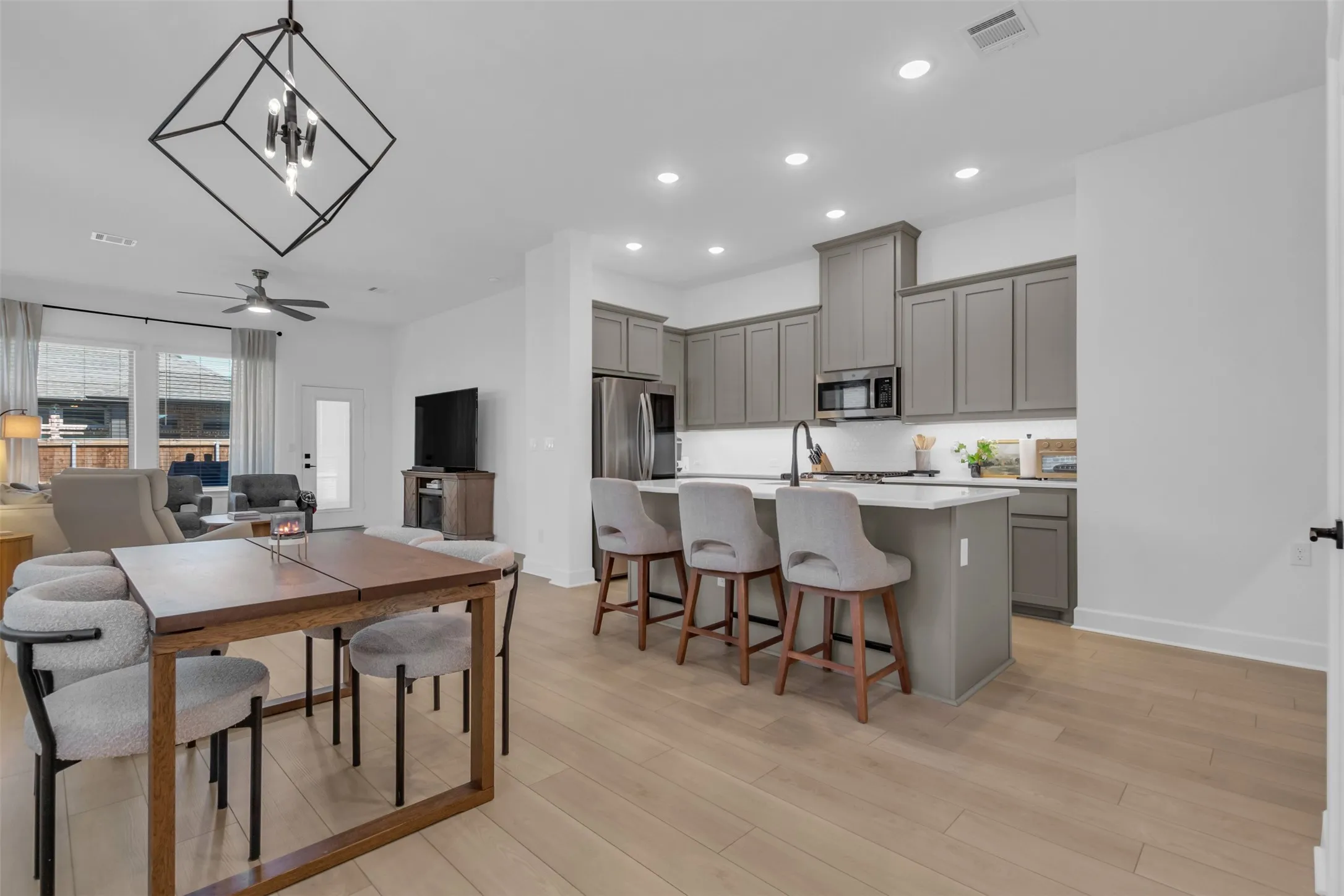 Open-concept living space featuring wood-finish flooring, a contemporary kitchen island with seating, recessed lighting, and a modern geometric chandelier