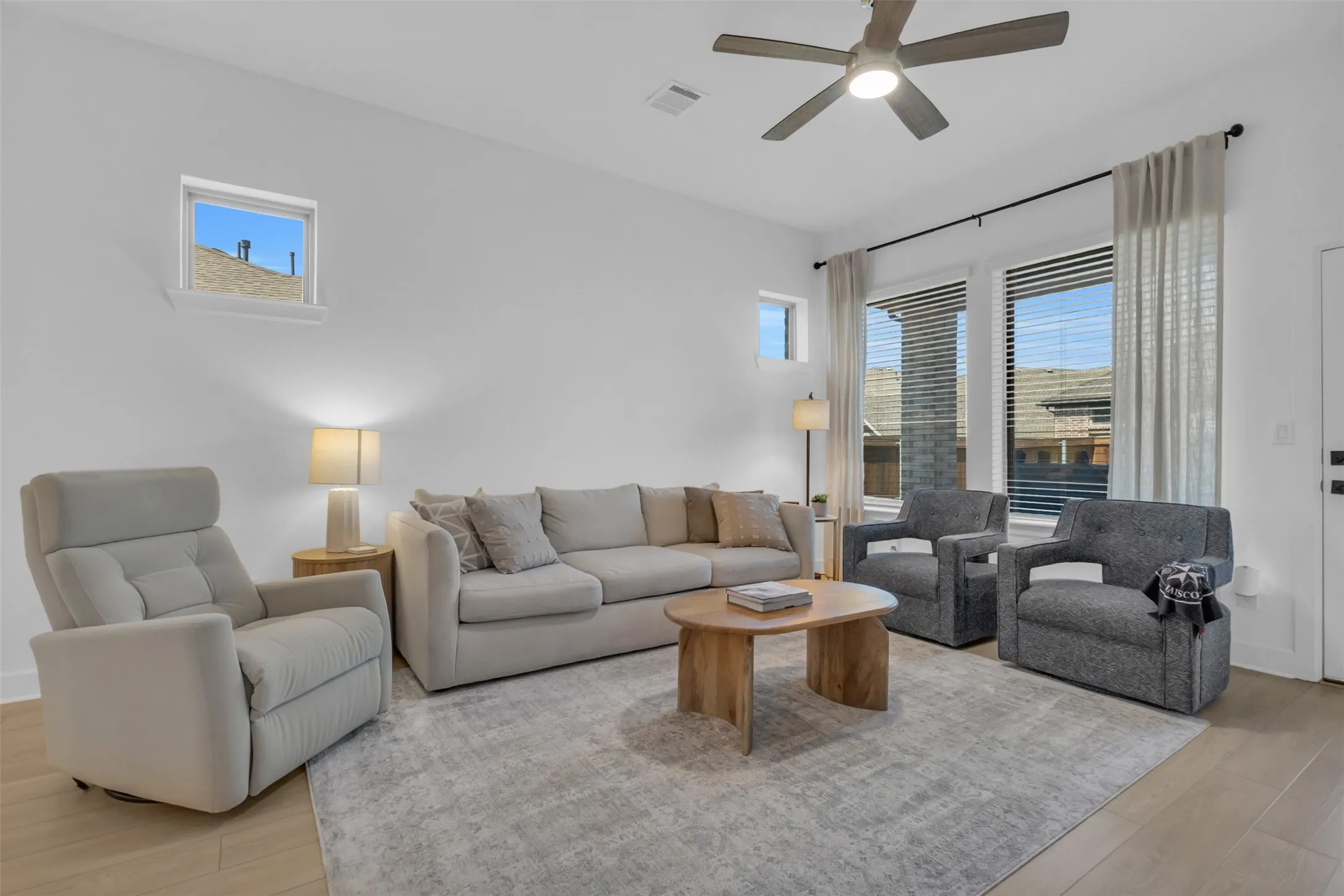 Spacious living area featuring light wood-finish flooring, white walls, and a contemporary ceiling fan