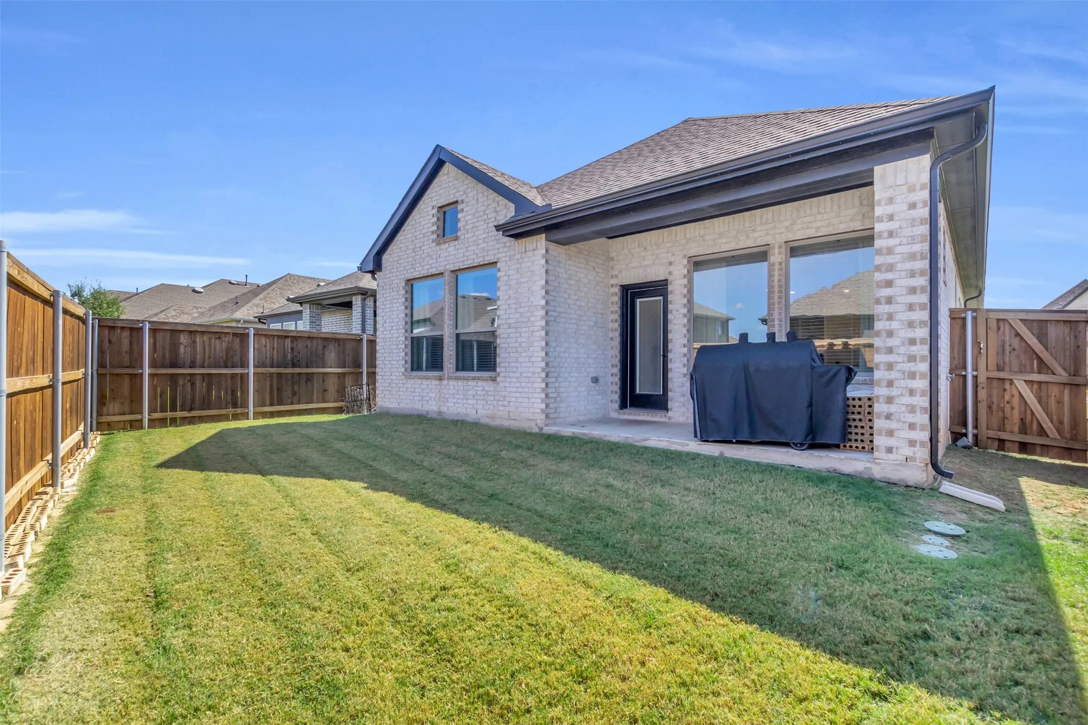 Expansive backyard with a manicured lawn, full privacy fencing, and a covered patio area