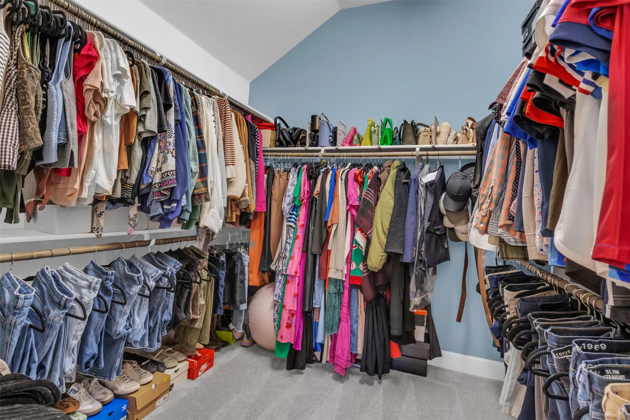 Custom-designed walk-in closet featuring extensive built-in shelving, multiple hanging rods, and sloped ceiling architecture