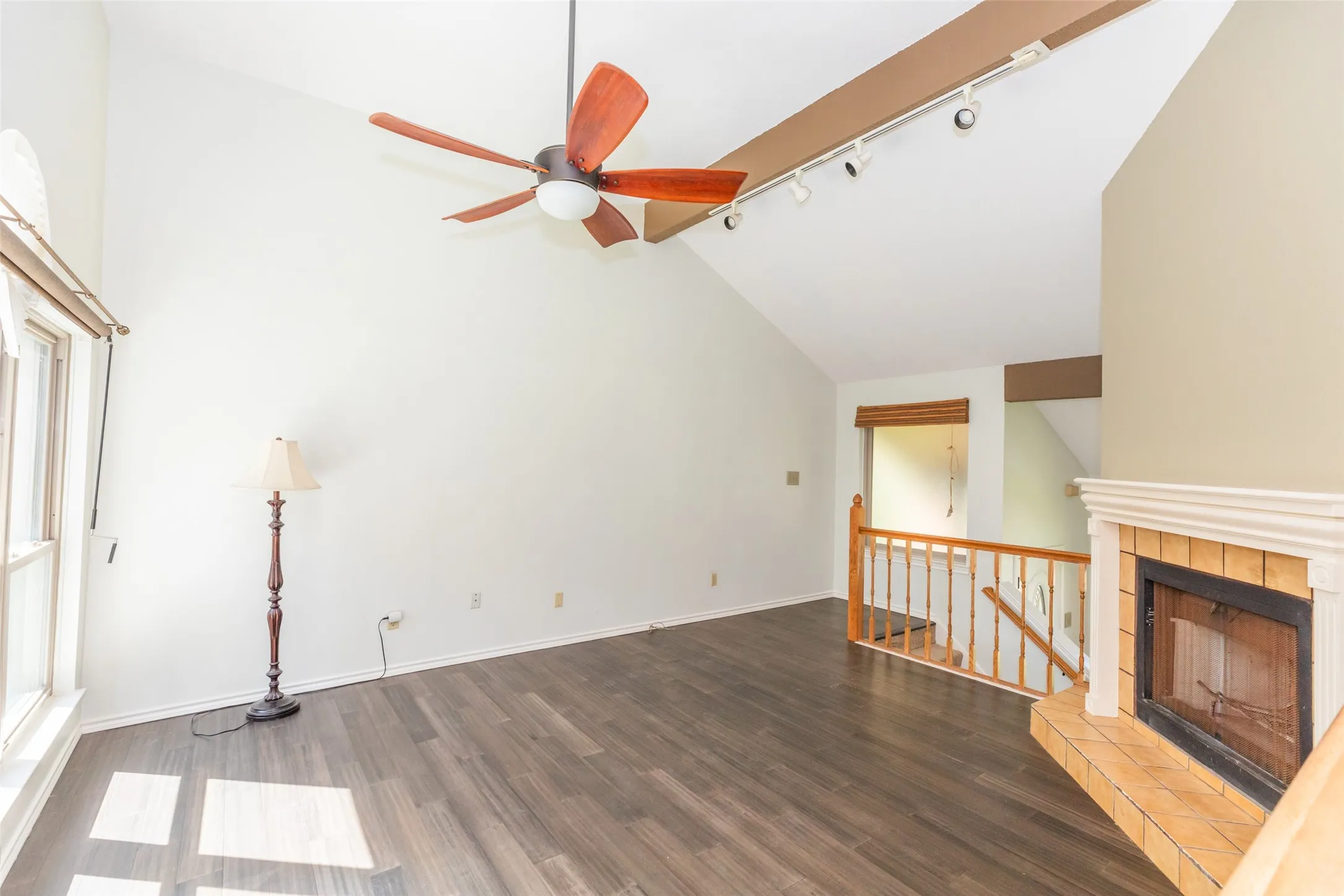 Living area featuring vaulted ceilings, wood-finish flooring, a fireplace with a tiled hearth, a wooden railing, and a ceiling fan