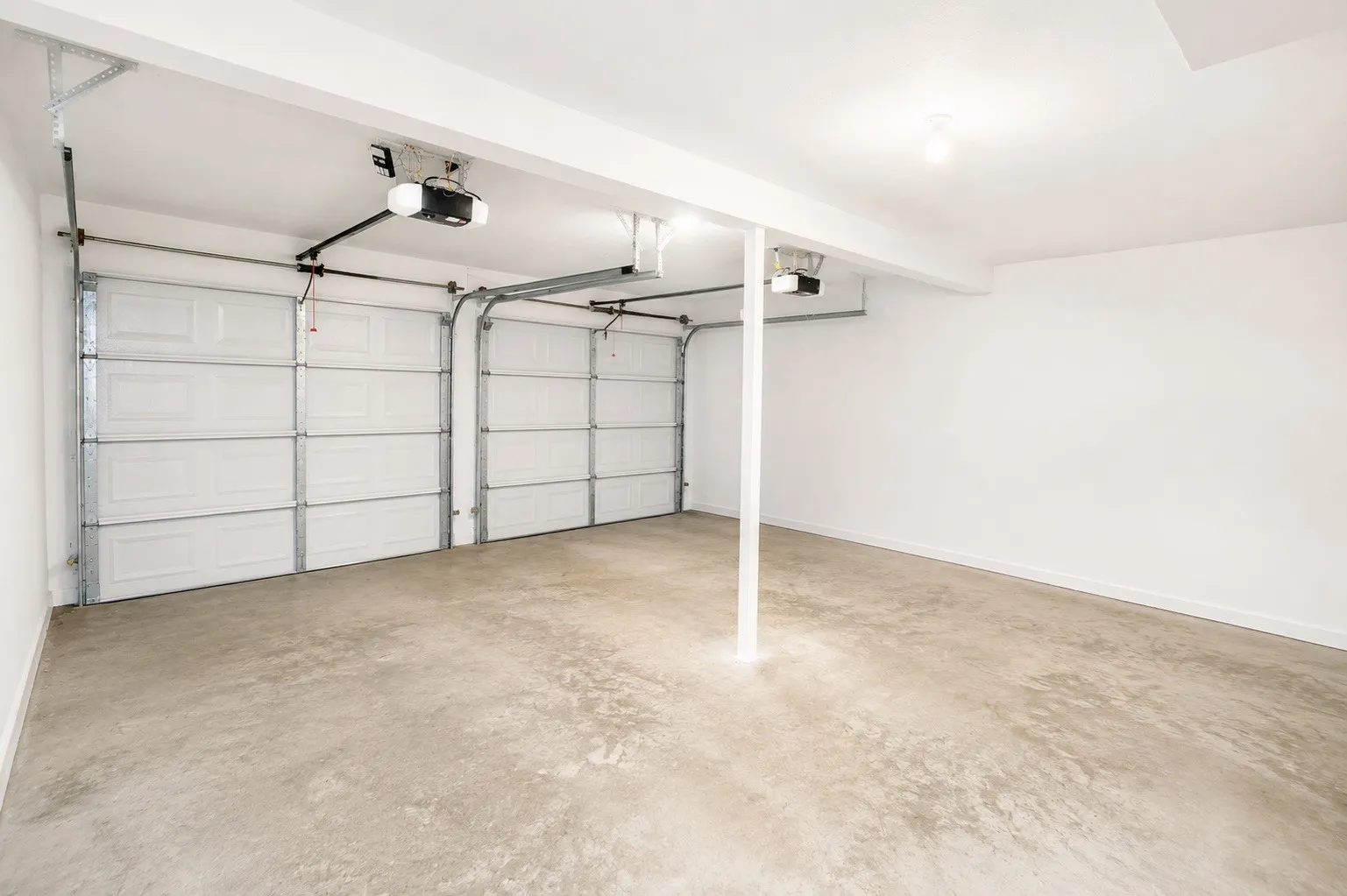 Spacious garage featuring two overhead doors, automatic openers, a concrete floor, painted white walls, and an exposed support beam