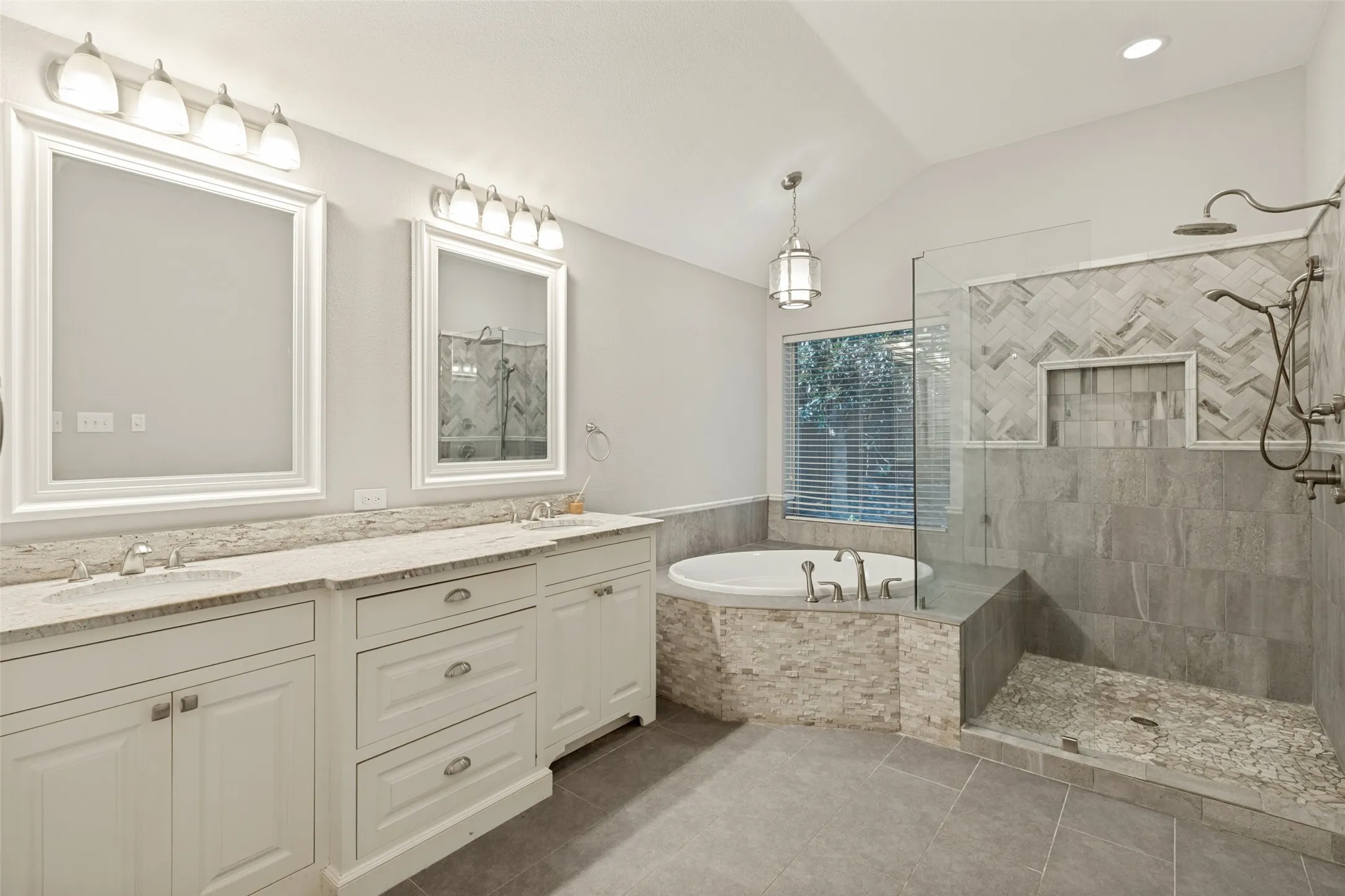 Dual sink vanity with stone countertops, soaking tub, glass-enclosed shower with tiled walls, and vaulted ceiling