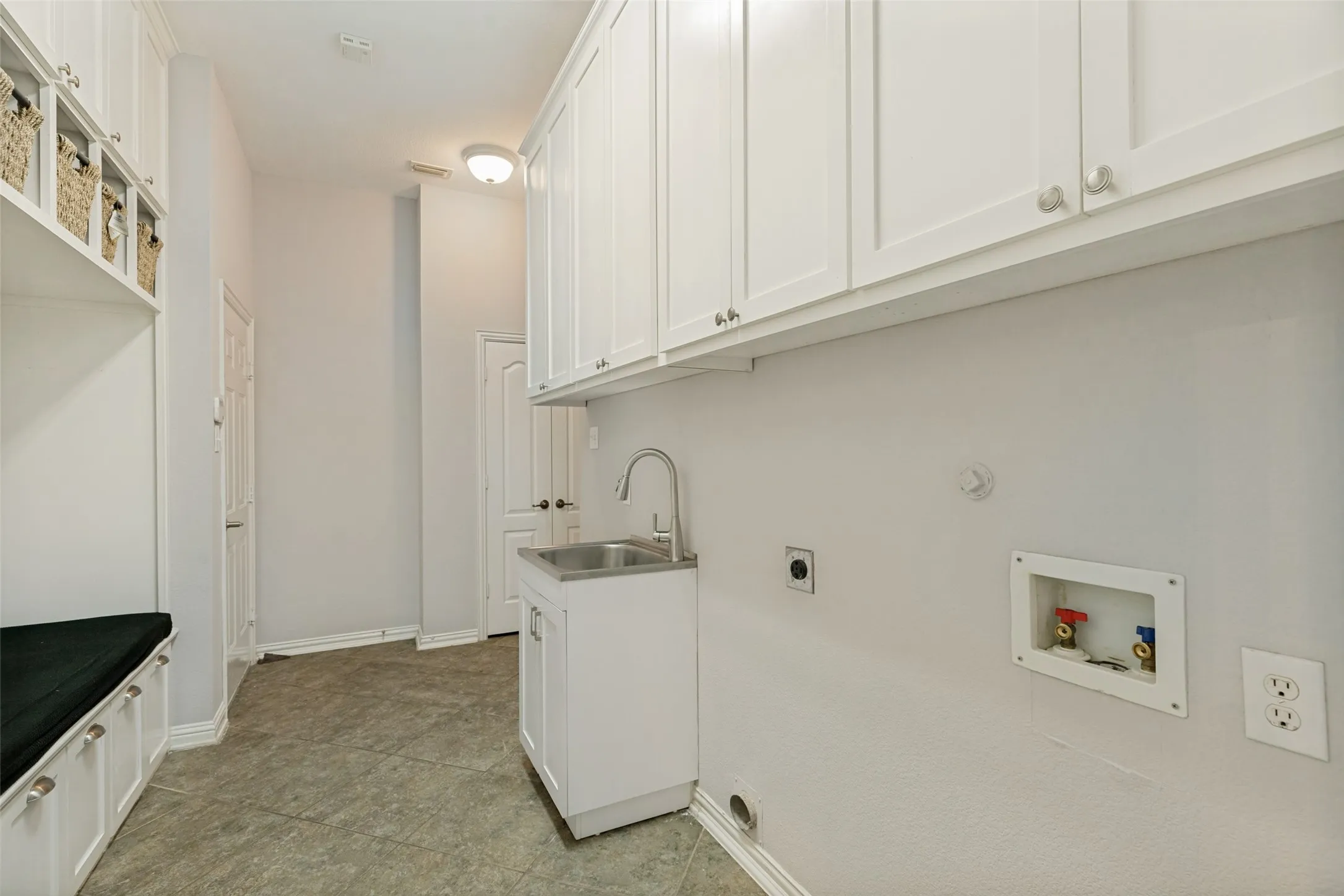 White shaker cabinetry, stainless steel utility sink, built-in storage bench, and gray tile flooring