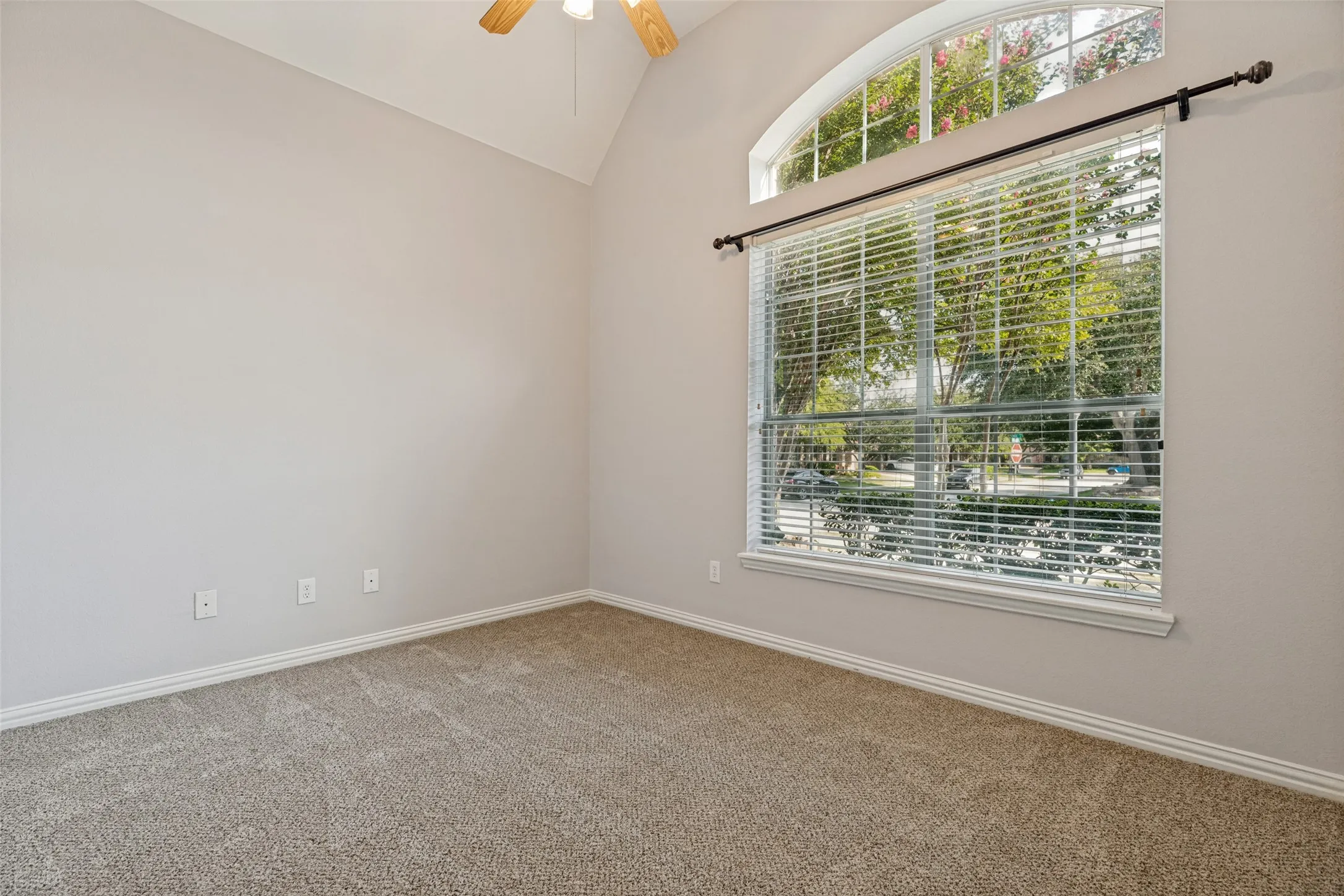 Vaulted ceiling with a ceiling fan, arched transom window, large window with blinds, and neutral carpeting
