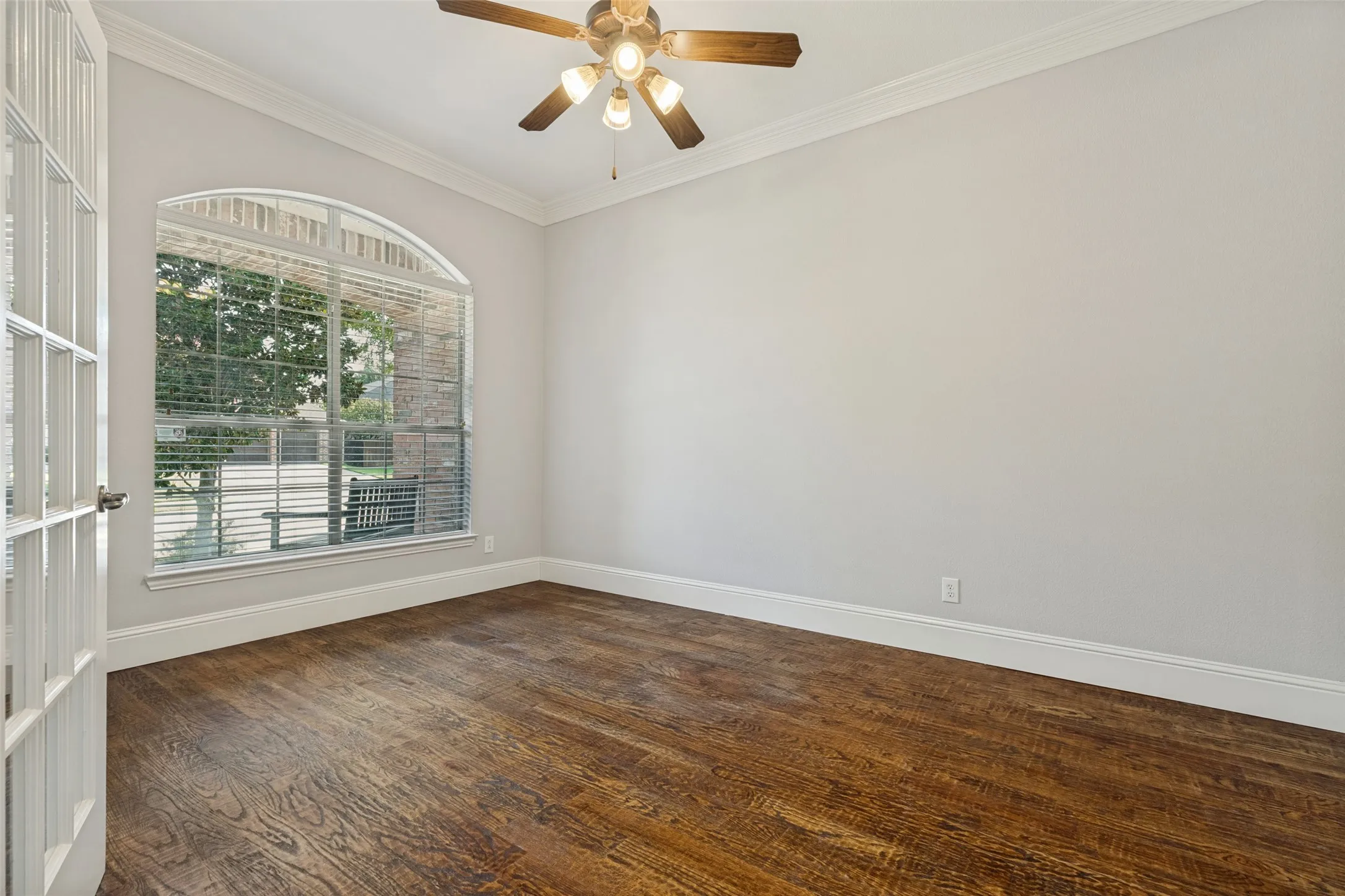 Wood-finish flooring, crown molding, arched window, ceiling fan, and French doors