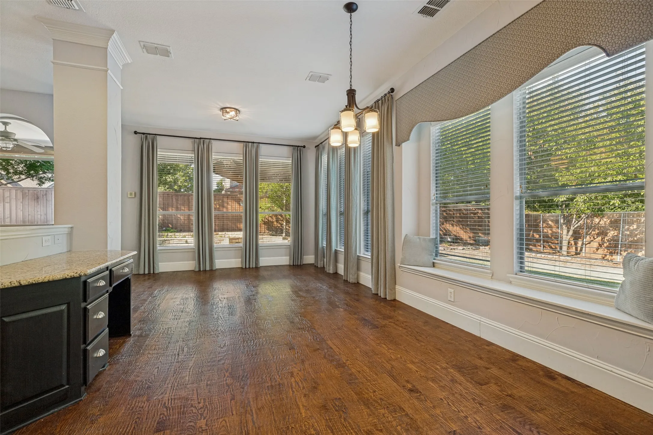 Wood-finish flooring, multiple windows, window seat, built-in cabinetry with stone countertop, and an overhead chandelier
