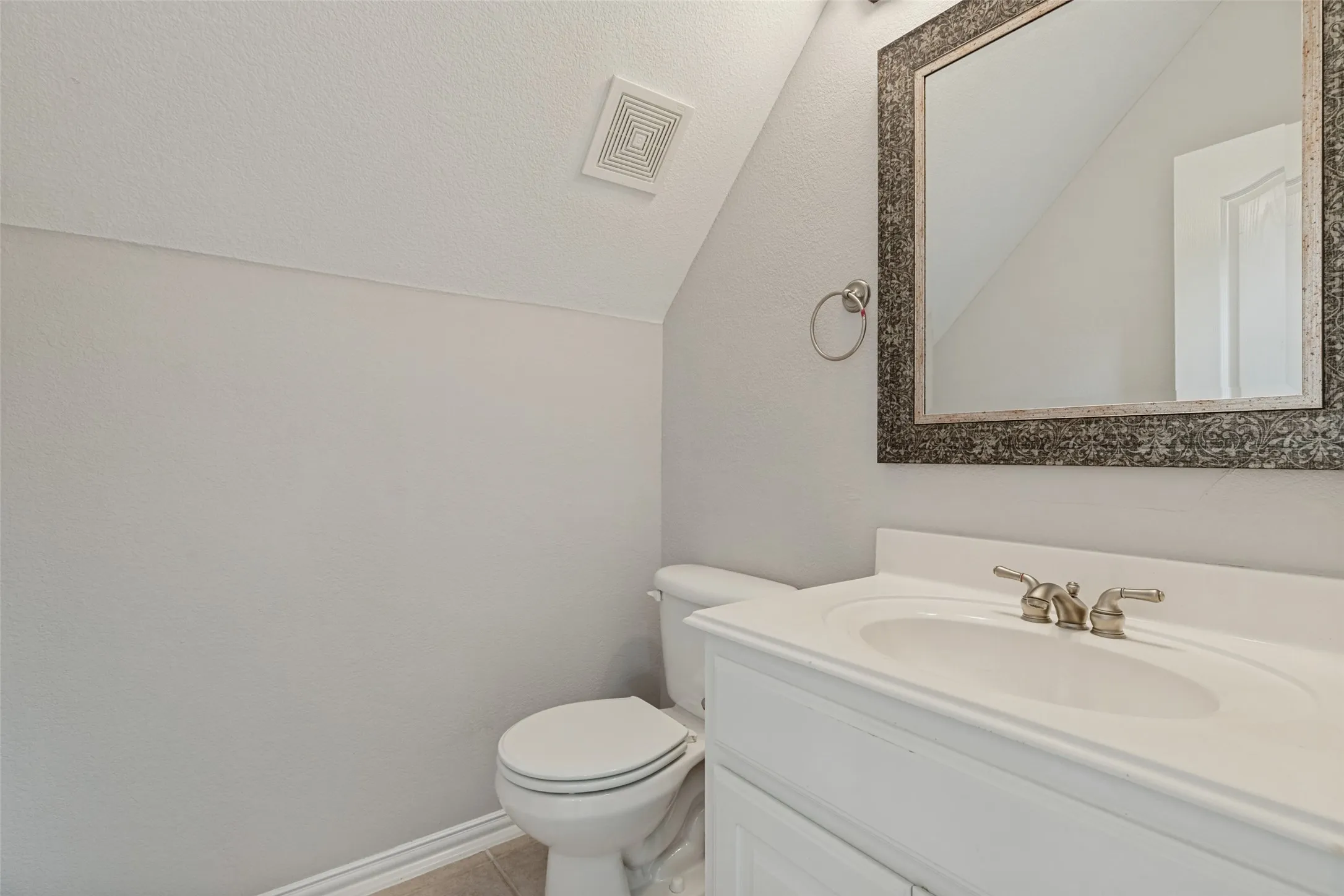 Clean and bright half bath featuring a white porcelain toilet, pedestal sink with chrome fixtures, and framed mirror with decorative border