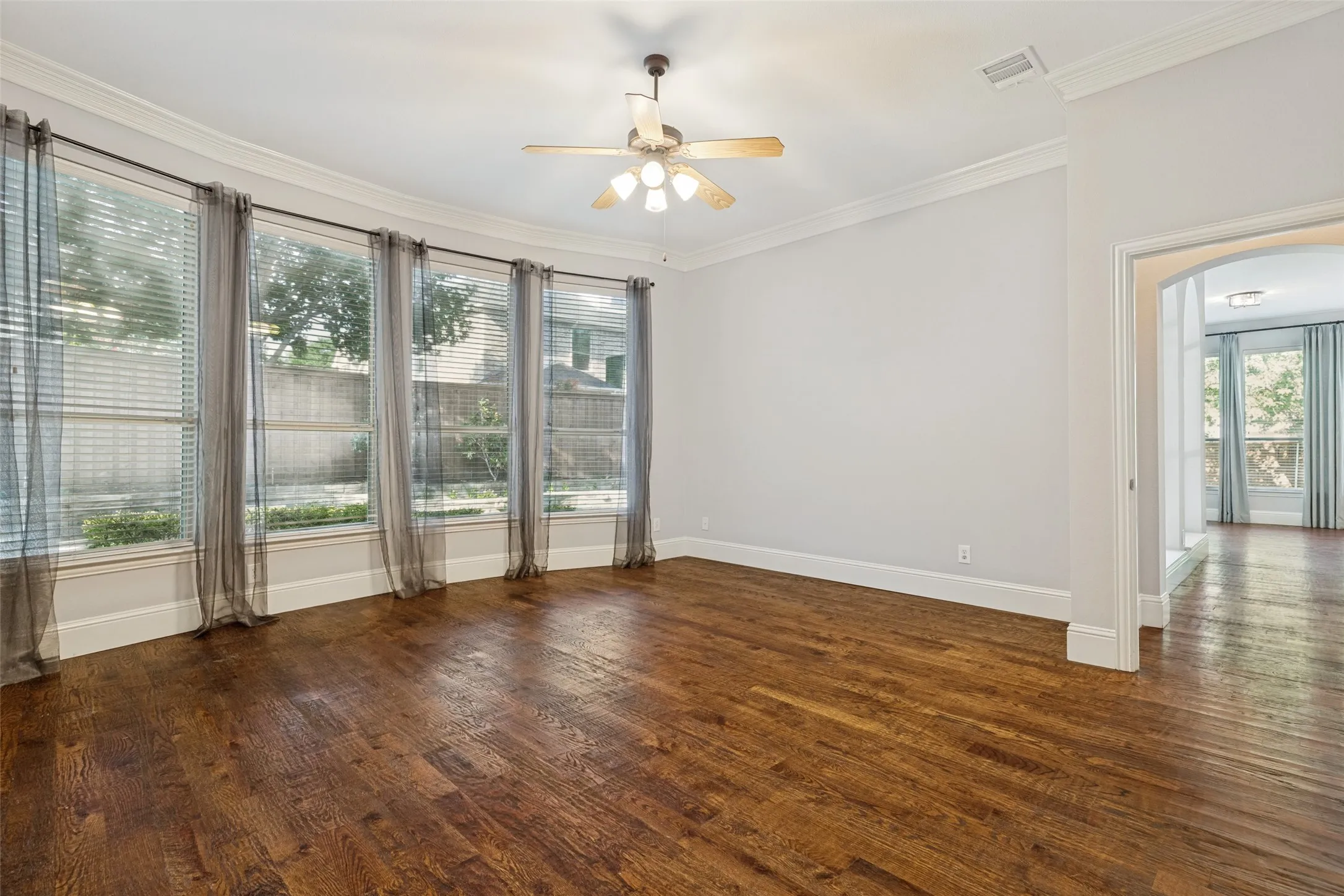 Hardwood flooring, multiple large windows, ceiling fan, crown molding, arched doorway