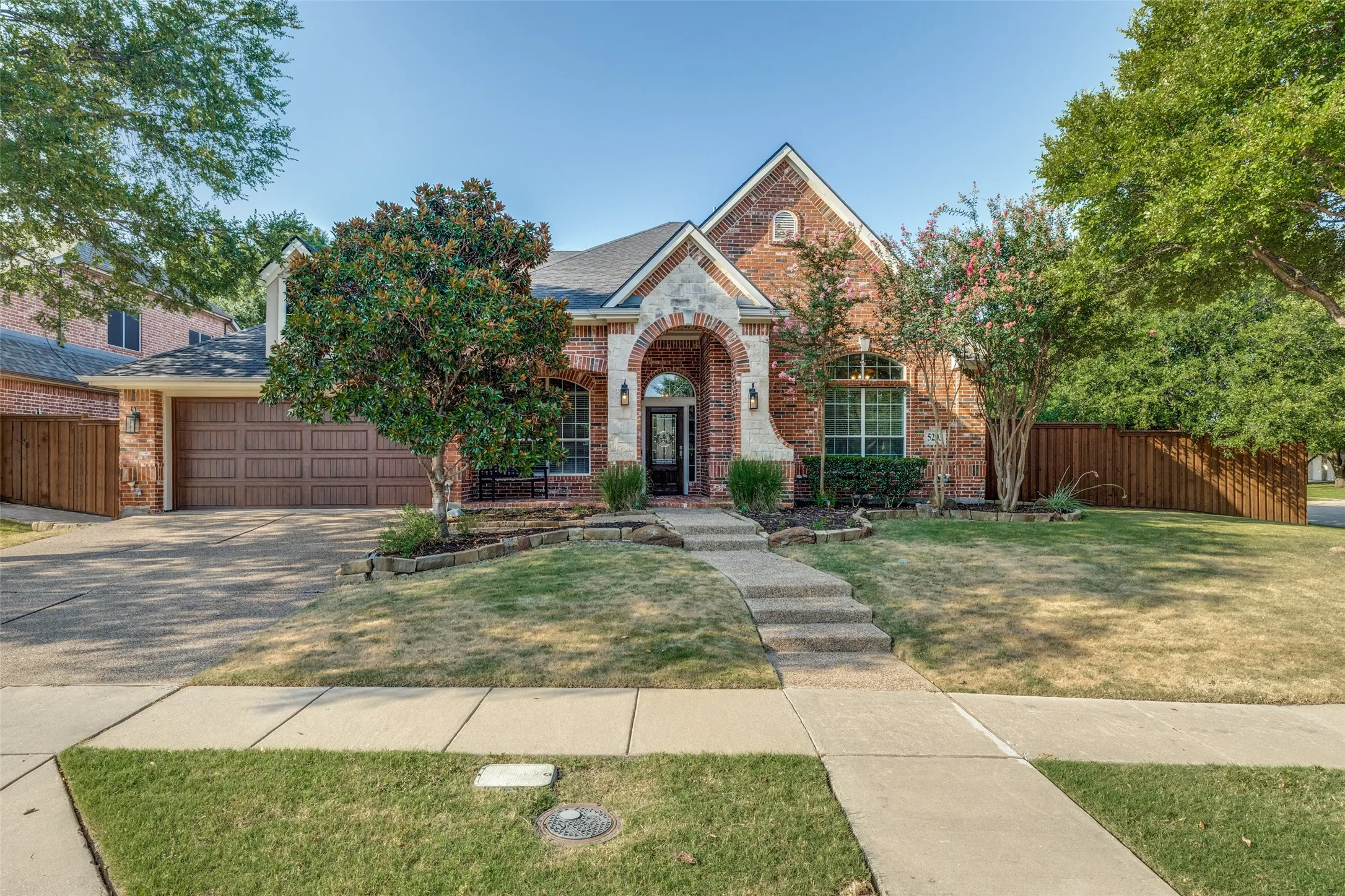 Brick exterior with stone accents, arched entry, gabled roofline, attached garage, and mature landscaping