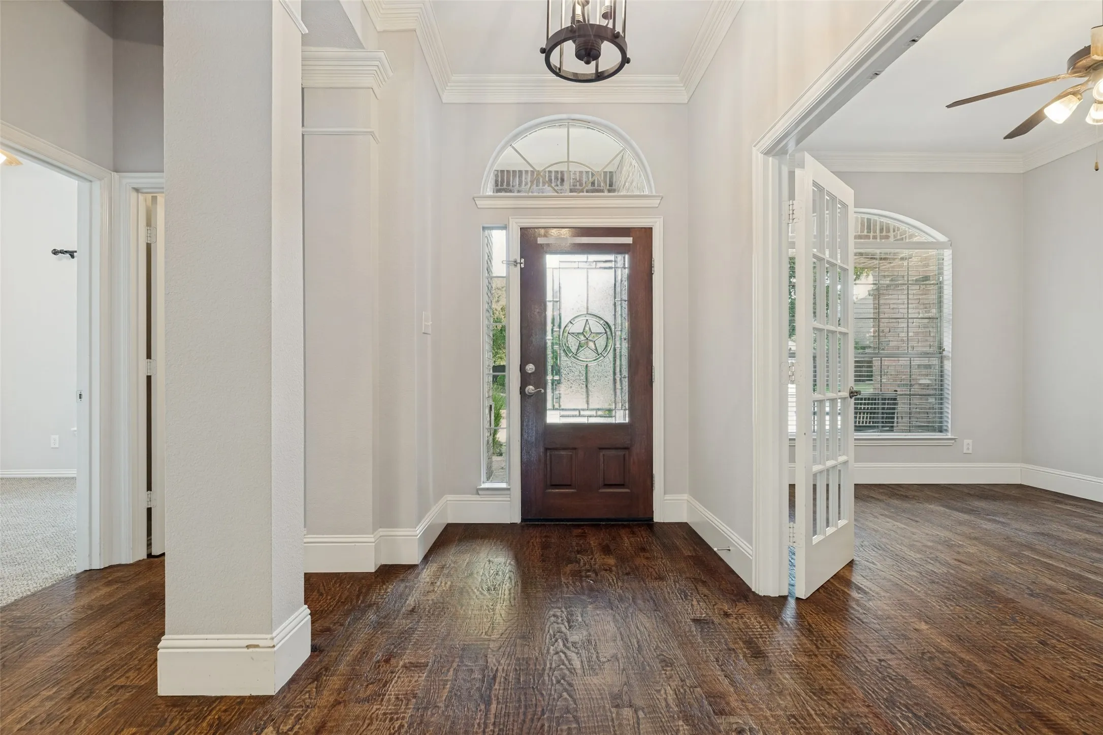 Hardwood flooring throughout, decorative entryway with leaded glass door, arched transom window, white French doors, and substantial crown molding