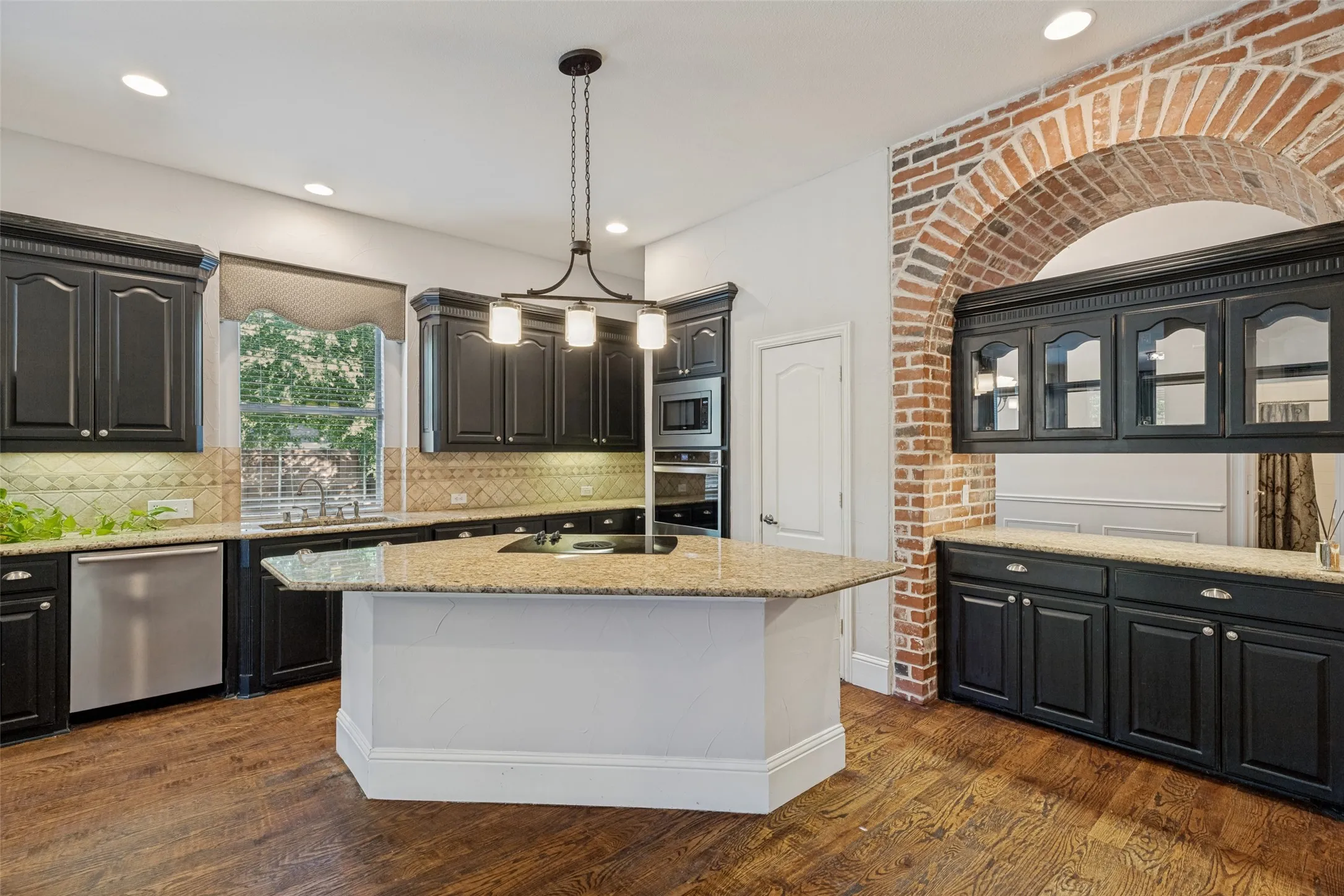 Kitchen featuring dark-finished cabinetry, granite countertops, stainless steel appliances, and a brick archway