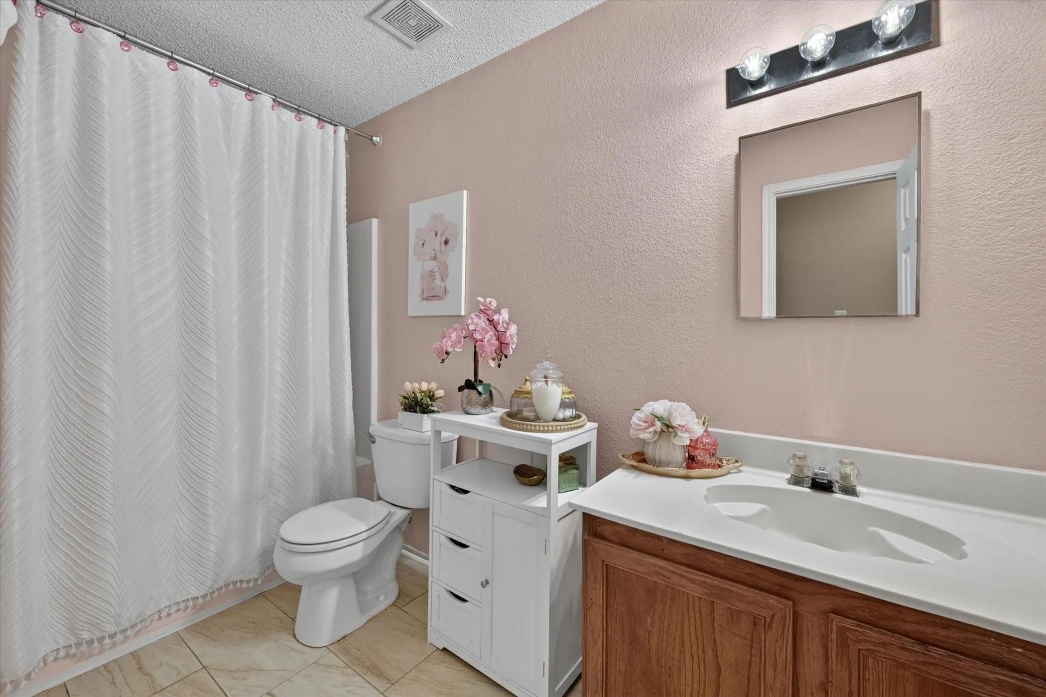 Bathroom featuring a single vanity with wood-finish cabinetry and a white countertop, a wall-mounted rectangular mirror, and a three-light vanity fixture
