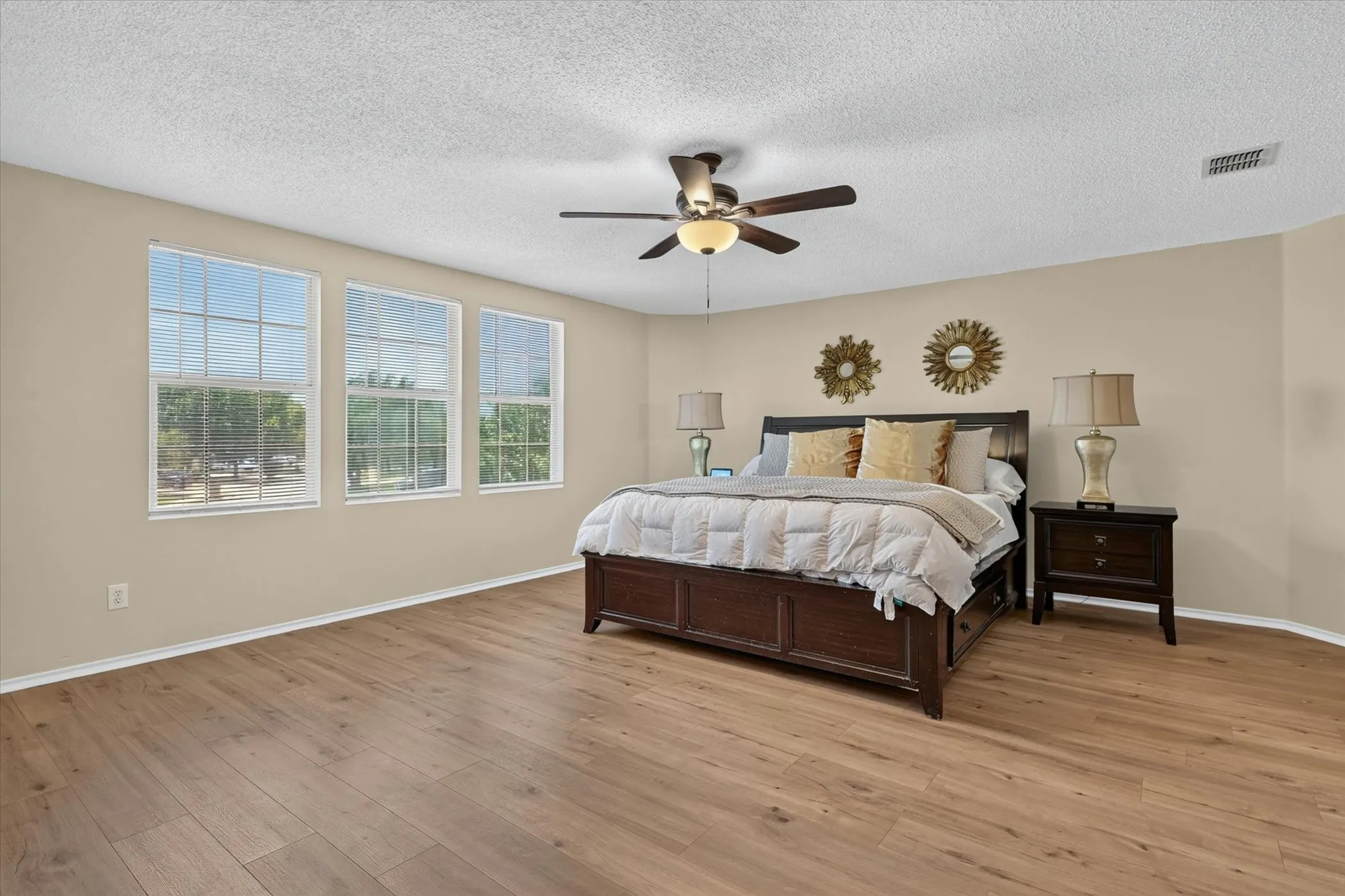 Spacious room featuring three large windows with white blinds, wood-finish flooring, and a ceiling fan with integrated lighting