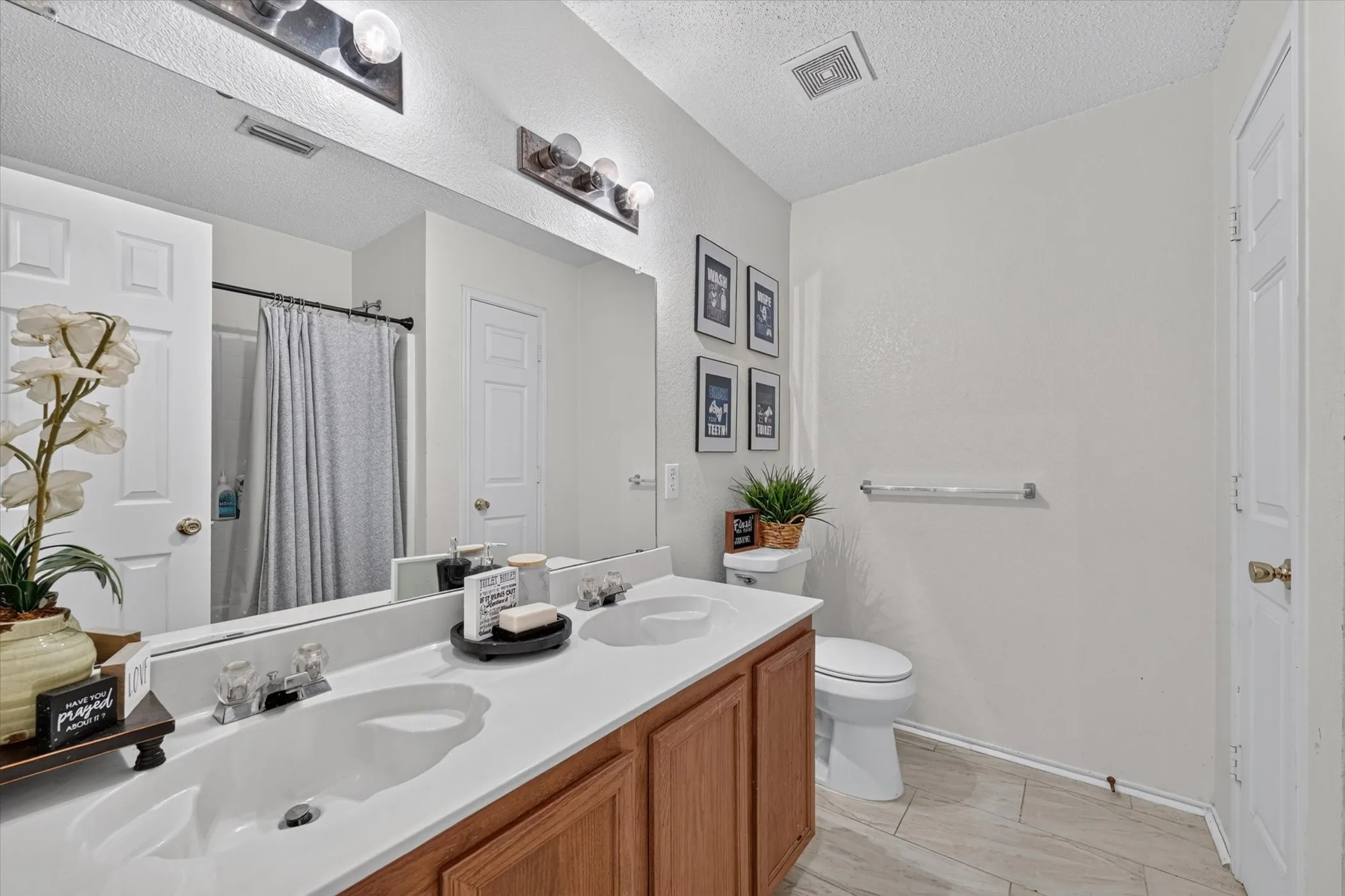 Bathroom featuring a double vanity with white countertops and wood-finish cabinetry, a large mirror, and overhead lighting