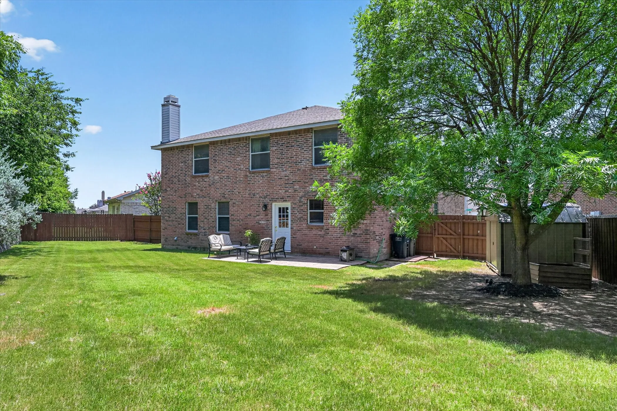 Expansive backyard featuring a manicured lawn, a large shade tree, and a concrete patio