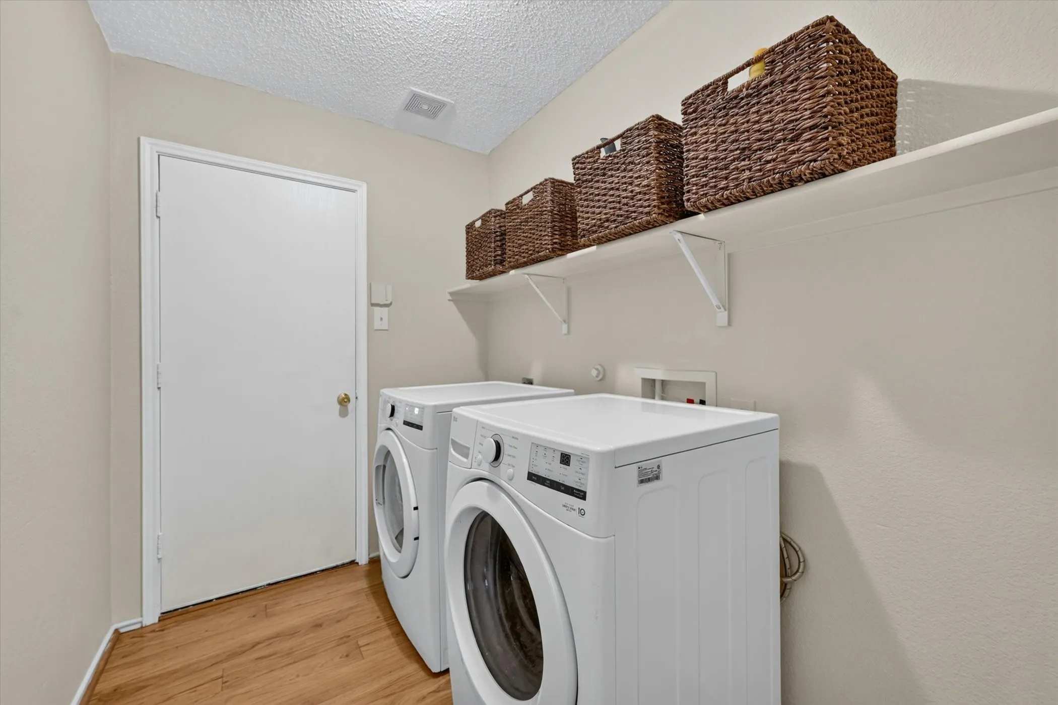 Dedicated laundry space featuring wood-finish flooring, light neutral wall tones, and a built-in wall shelf with brackets